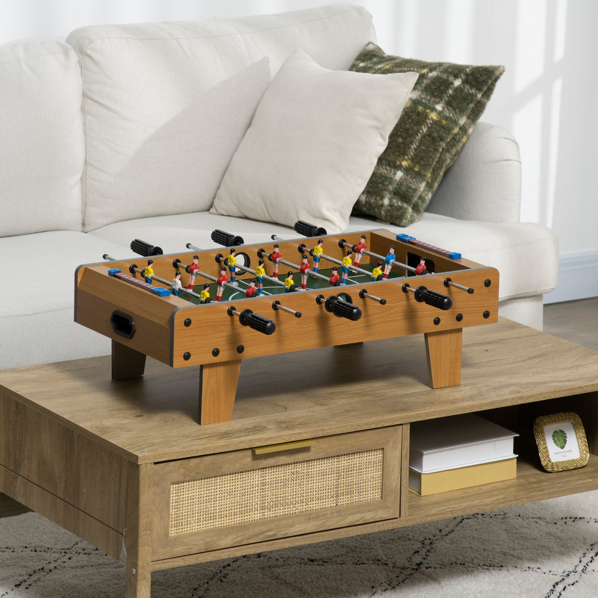 Mesa de futbolín sobre una mesa de centro en una sala de estar con un sofá y almohadas.