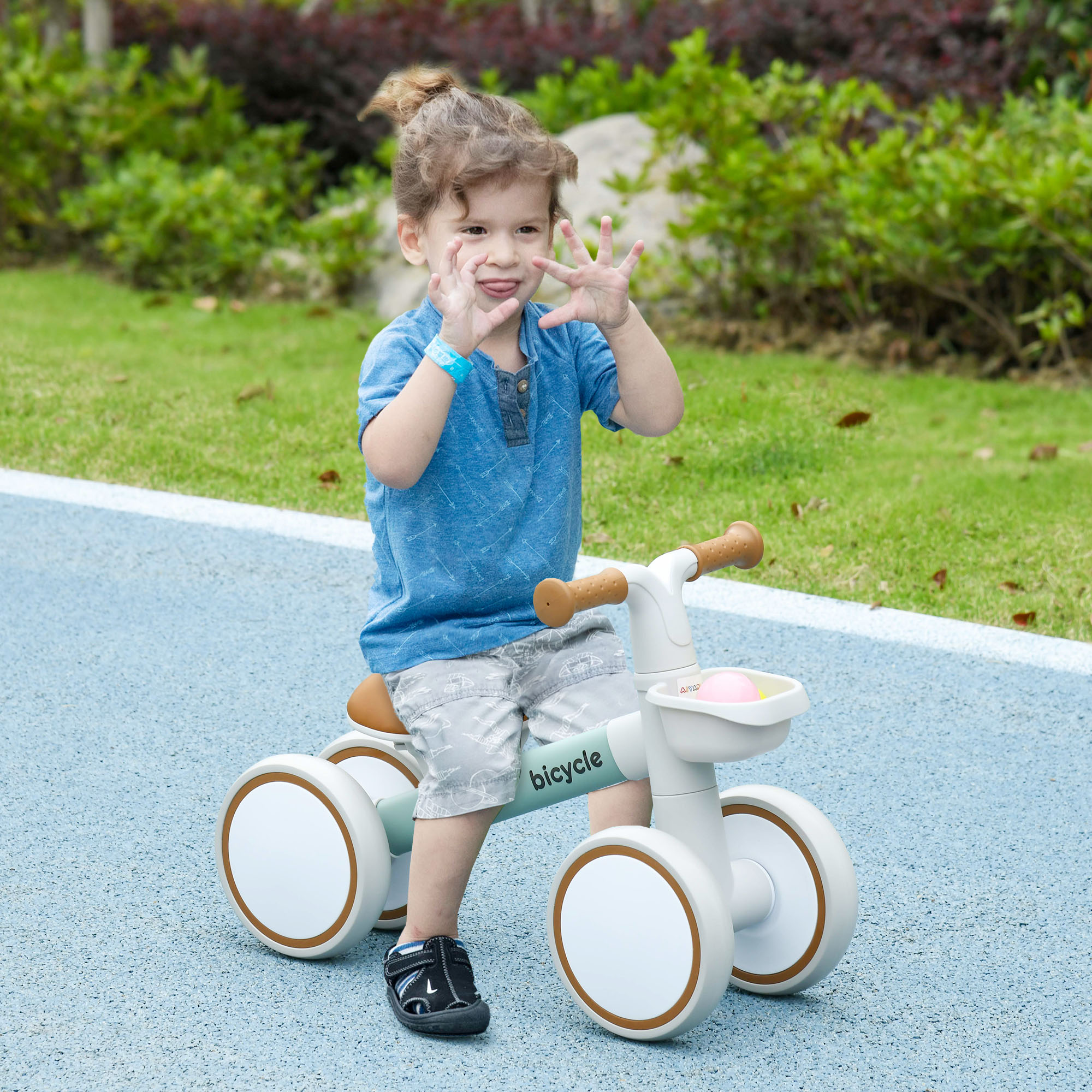 Niño en bicicleta de equilibrio, camino azul. Niño sonriendo y sacando la lengua. Hierba verde al fondo.