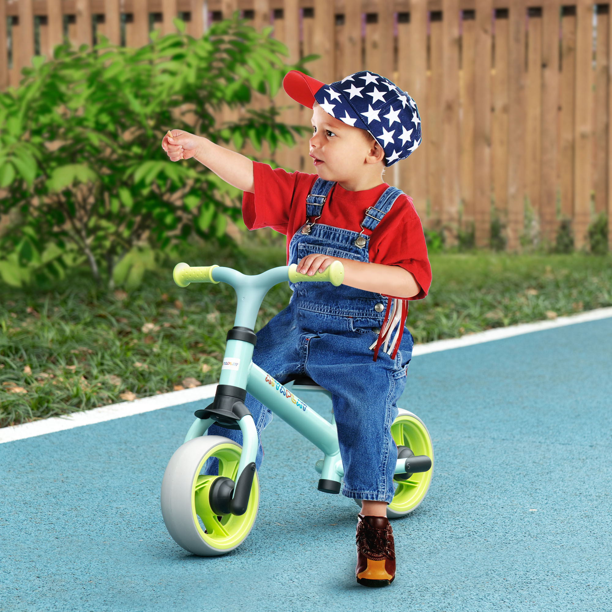 Un niño pequeño montando en una bicicleta sin pedales. El niño lleva gorro, camisa roja y peto azul.