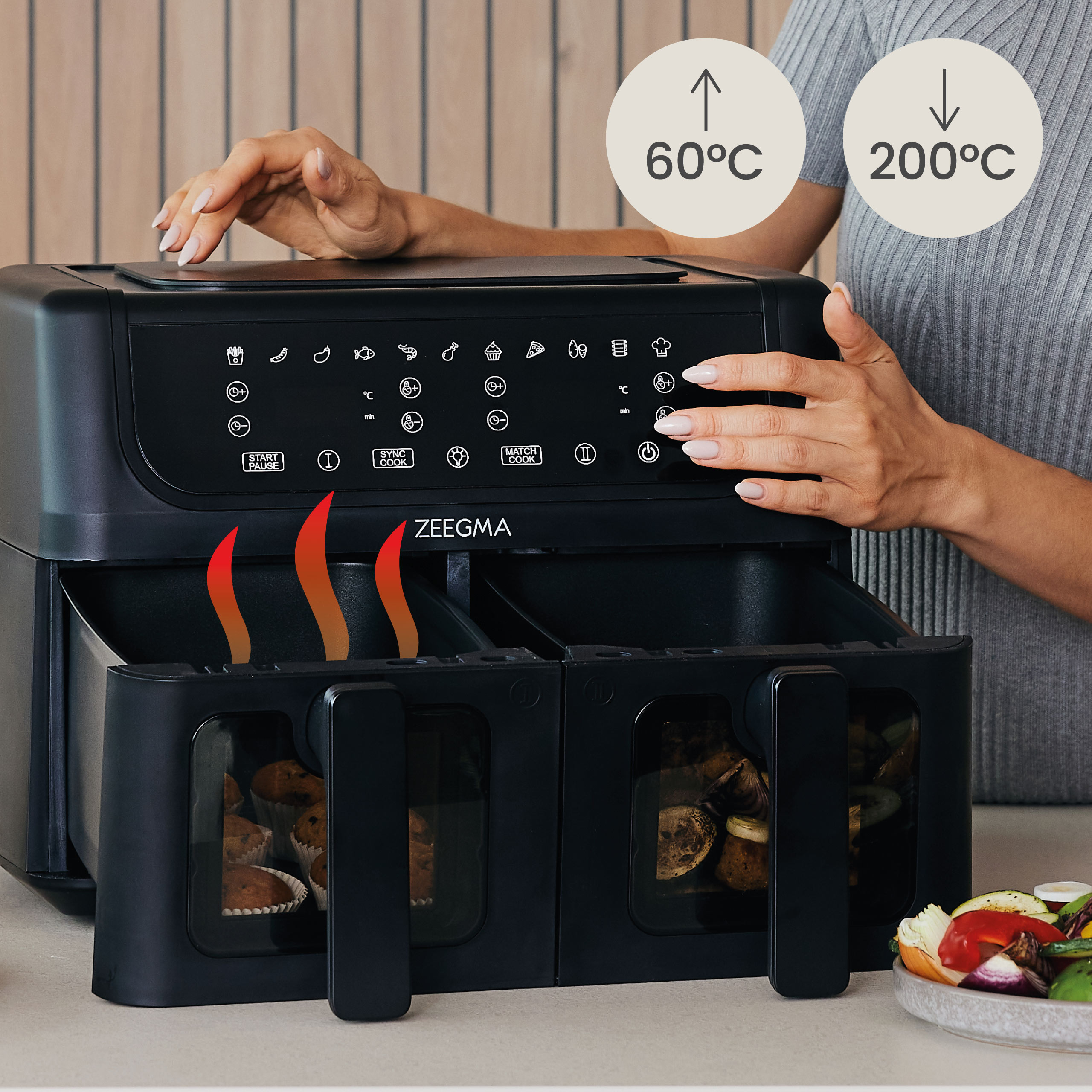 Een airfryer met twee compartimenten. De handen van een vrouw bevinden zich in de buurt van de bovenkant. Temperaturen worden aangegeven.