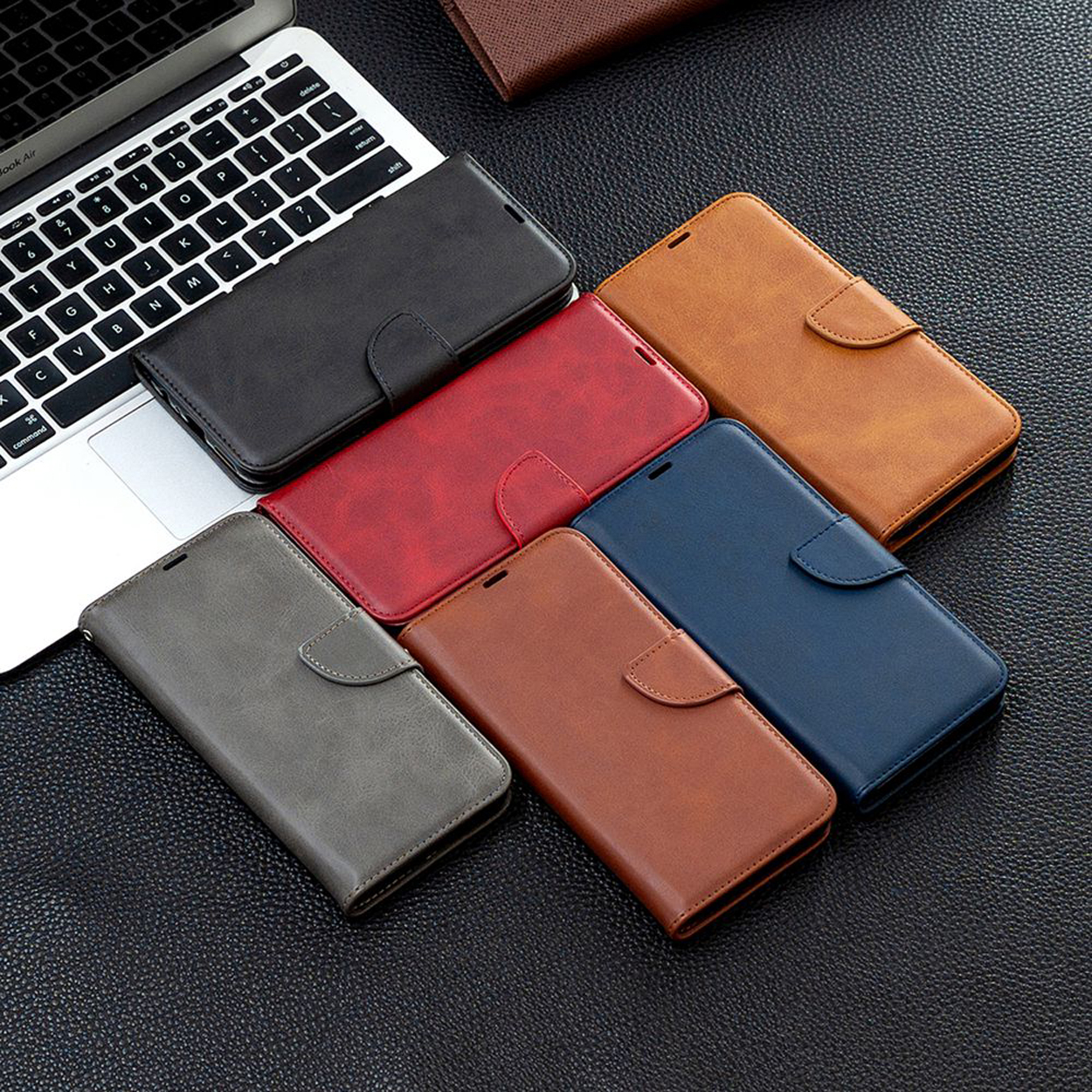 Verschillende leren telefoonhoesjes in meerdere kleuren, met een laptop. De hoesjes liggen op een zwart oppervlak.