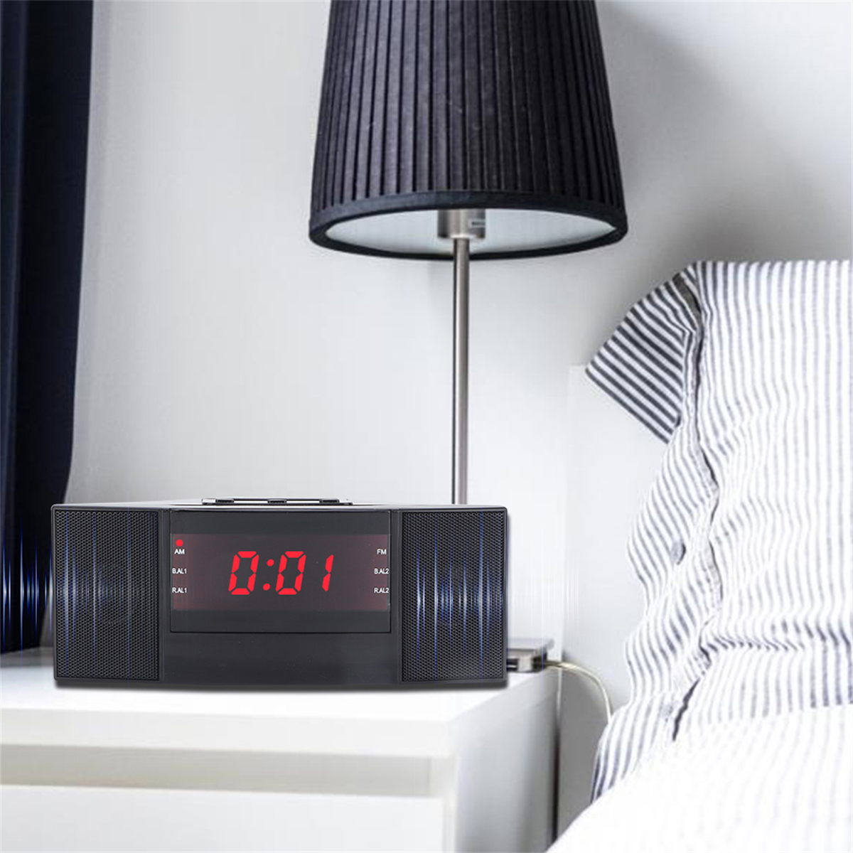 Schwarze Digitaluhr auf einem weißen Nachttisch. Links ist eine Lampe. Die Uhrzeit ist 0:01.