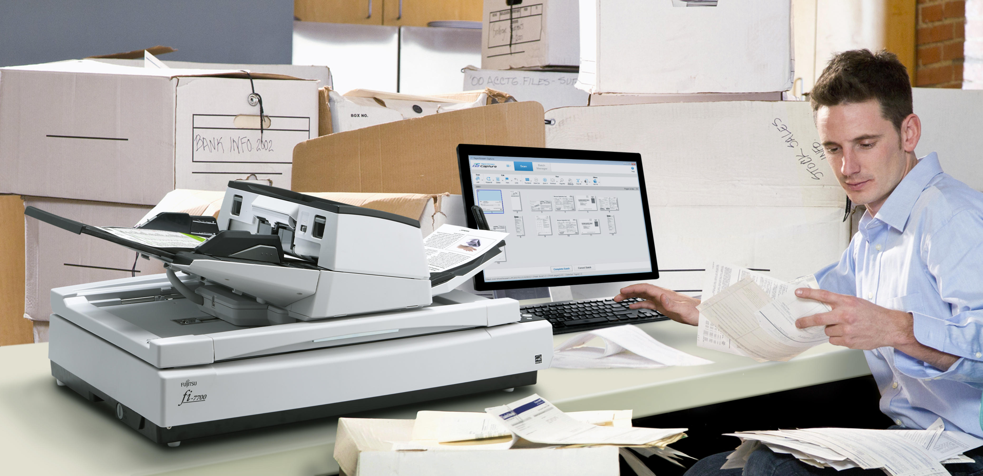 Un uomo lavora a una scrivania con un computer e uno scanner, ordinando documenti.