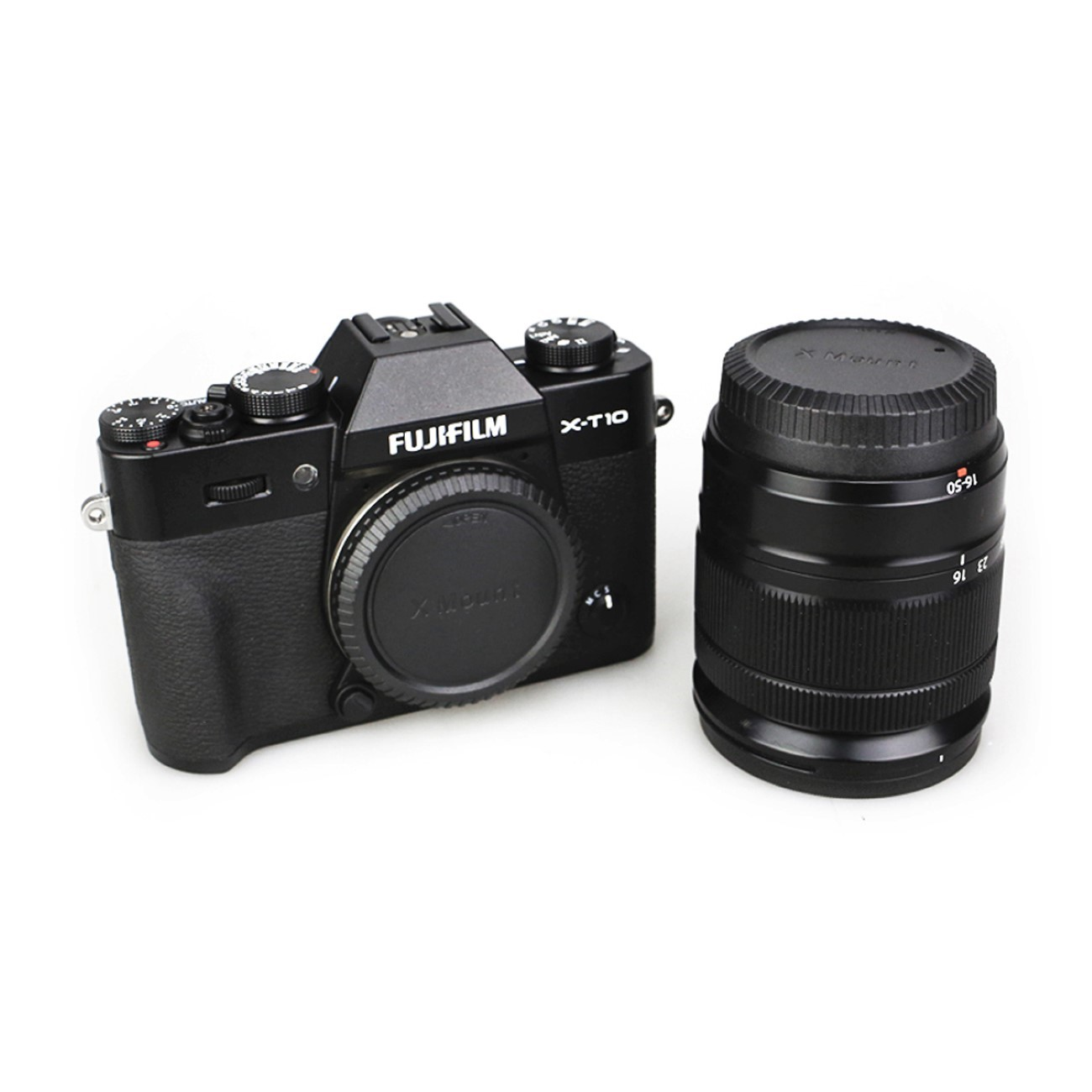 Schwarze Fujifilm X-T10 Kamera mit Objektiv. Das Objektiv befindet sich neben der Kamera. Beide auf weißer Oberfläche.