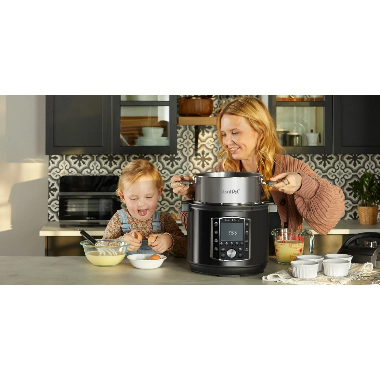 Vrouw en kind aan het koken. Een zwarte Instant Pot staat op het aanrecht, omringd door ingrediënten.