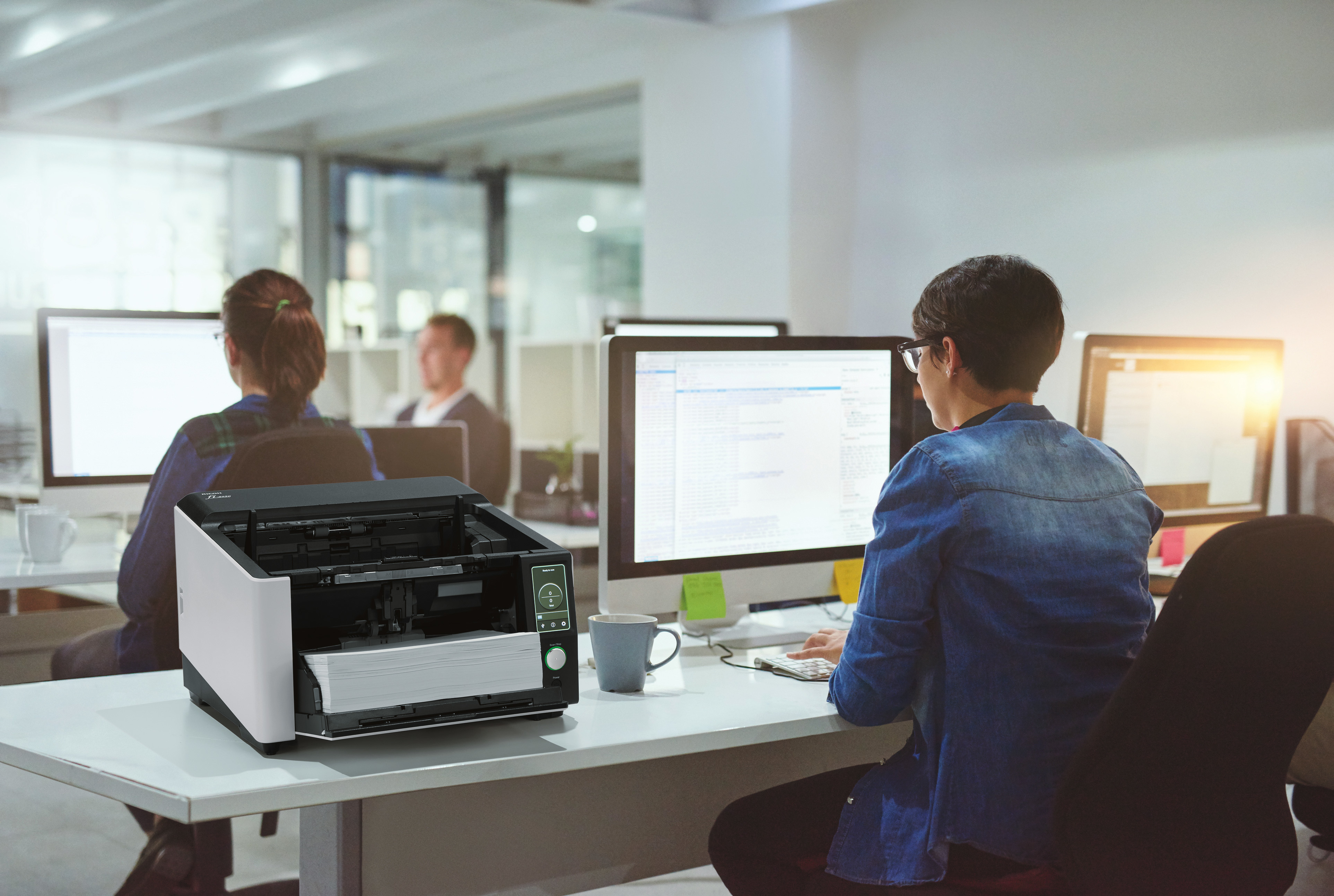 Kantoor met mensen die aan computers werken en een scanner met documenten.