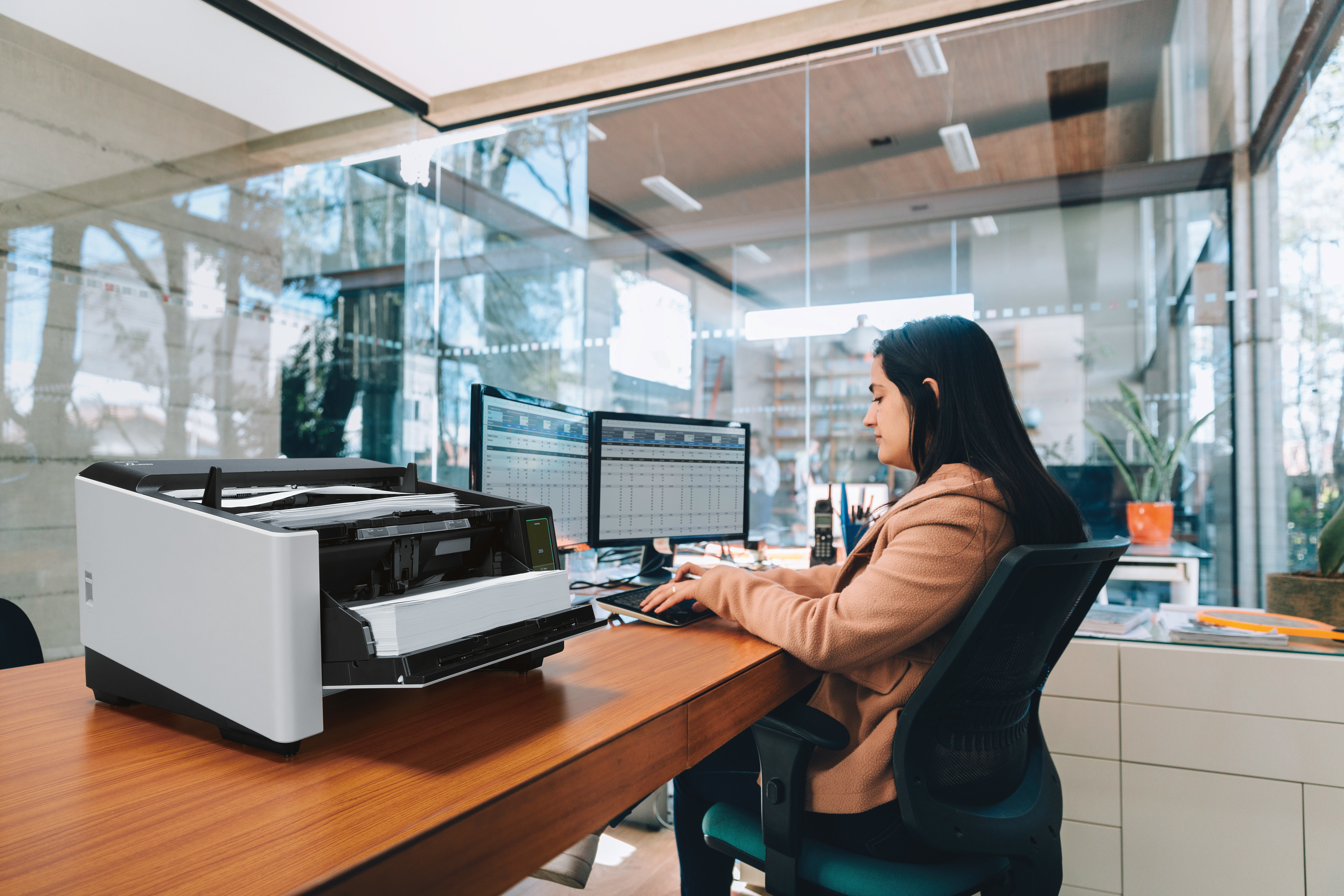 Vrouw die werkt aan een bureau met computer en scanner.