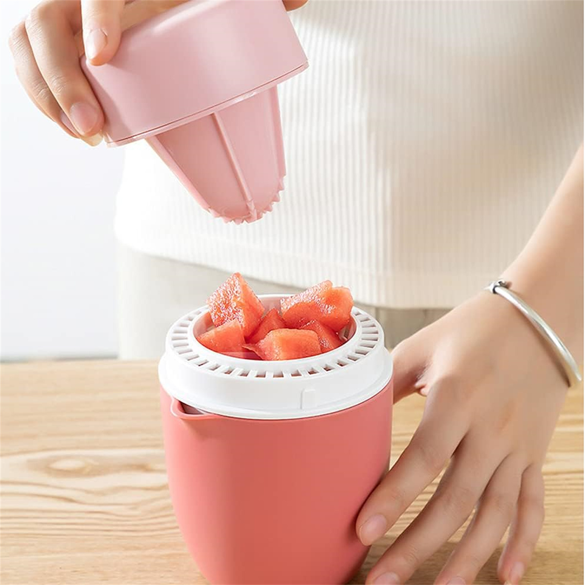 Ein rosa Wassermelonen-Schneider. Wassermelonenwürfel darin, und der Deckel wird von einer Hand entfernt.