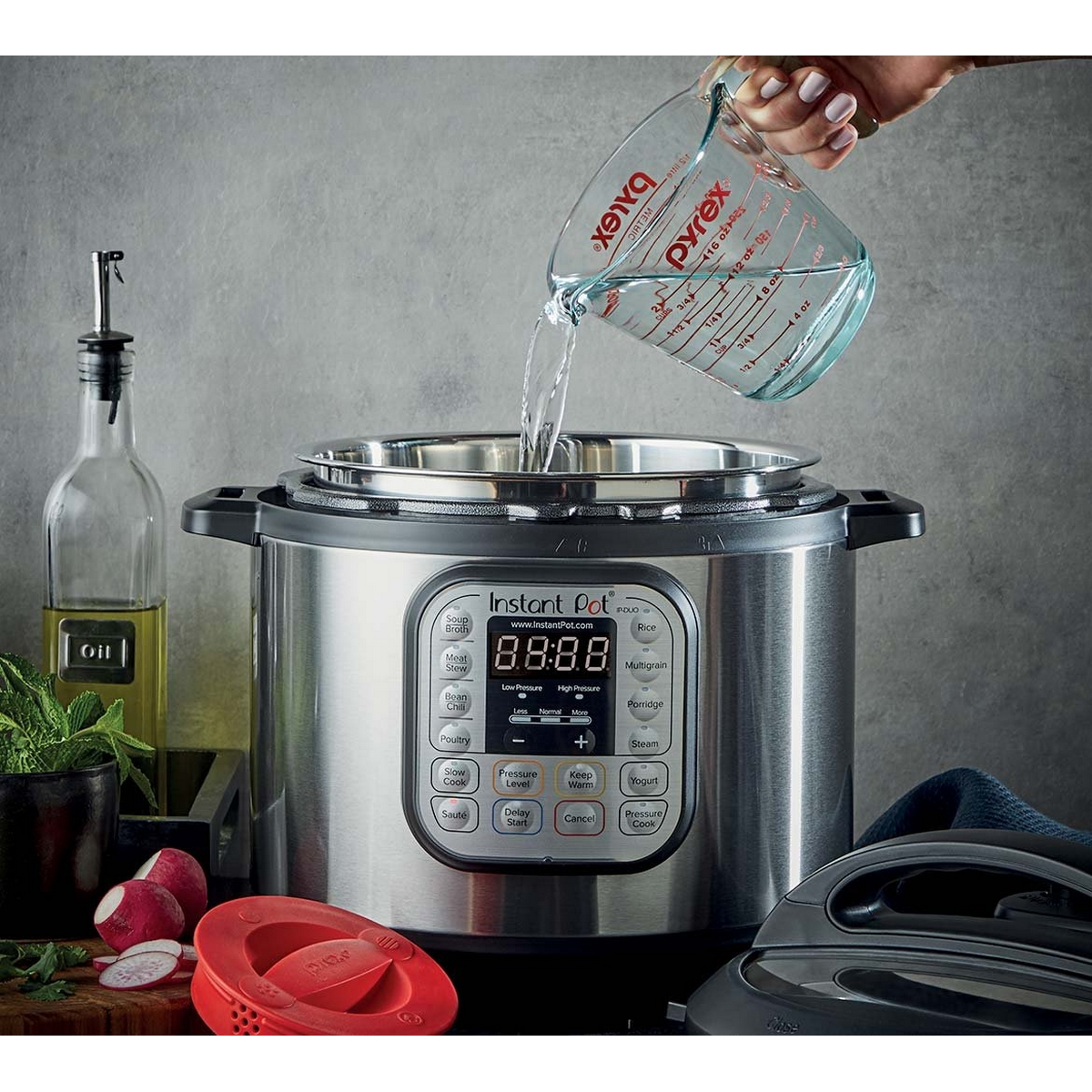 Un Instant Pot viene riempito con acqua da un misurino Pyrex. Davanti ci sono ravanelli e una bottiglia d'olio.