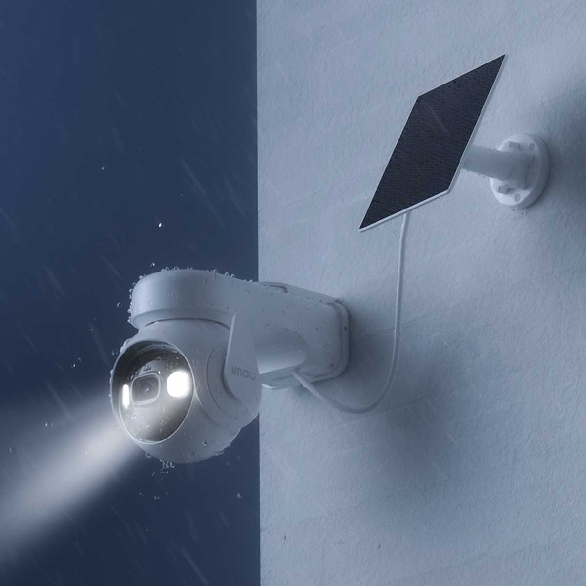 Biała kamera bezpieczeństwa z panelem słonecznym, zamontowana na ścianie w deszczu.