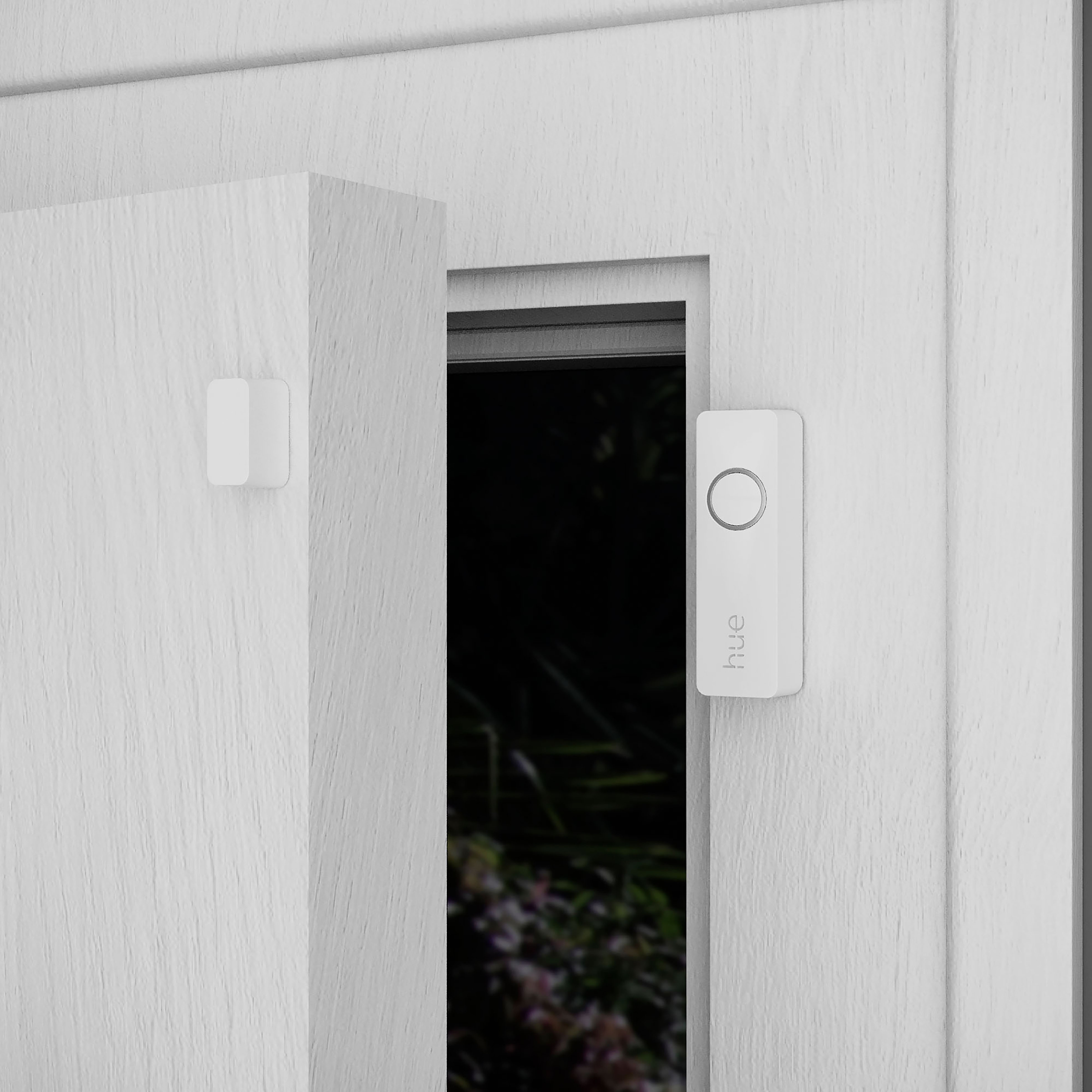 Porte et cadre blancs avec une sonnette blanche à droite et un capteur à gauche. Fond sombre.