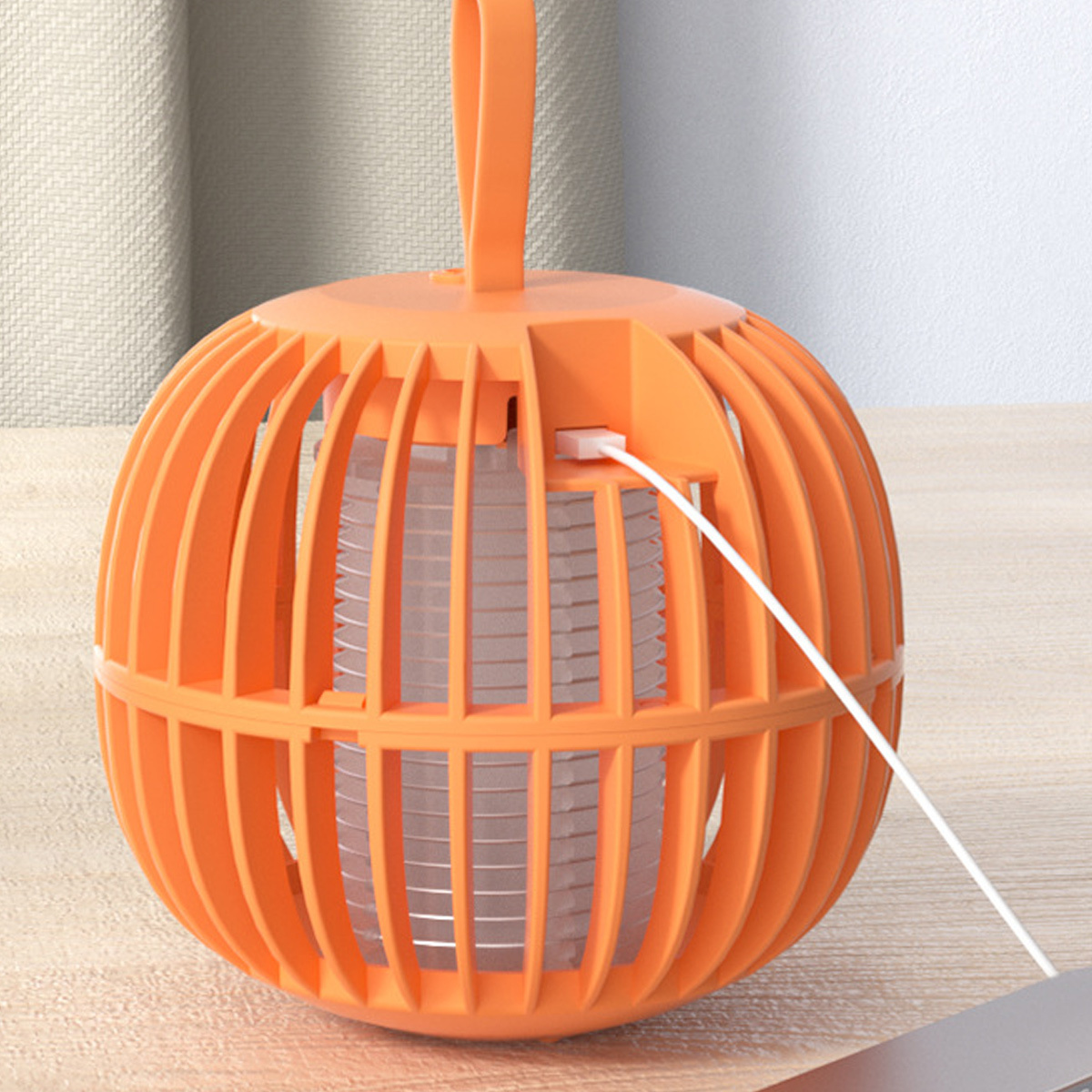 Eine orangefarbene, kugelförmige Mückenfalle mit Ladekabel. Sie steht auf einem Holztisch.