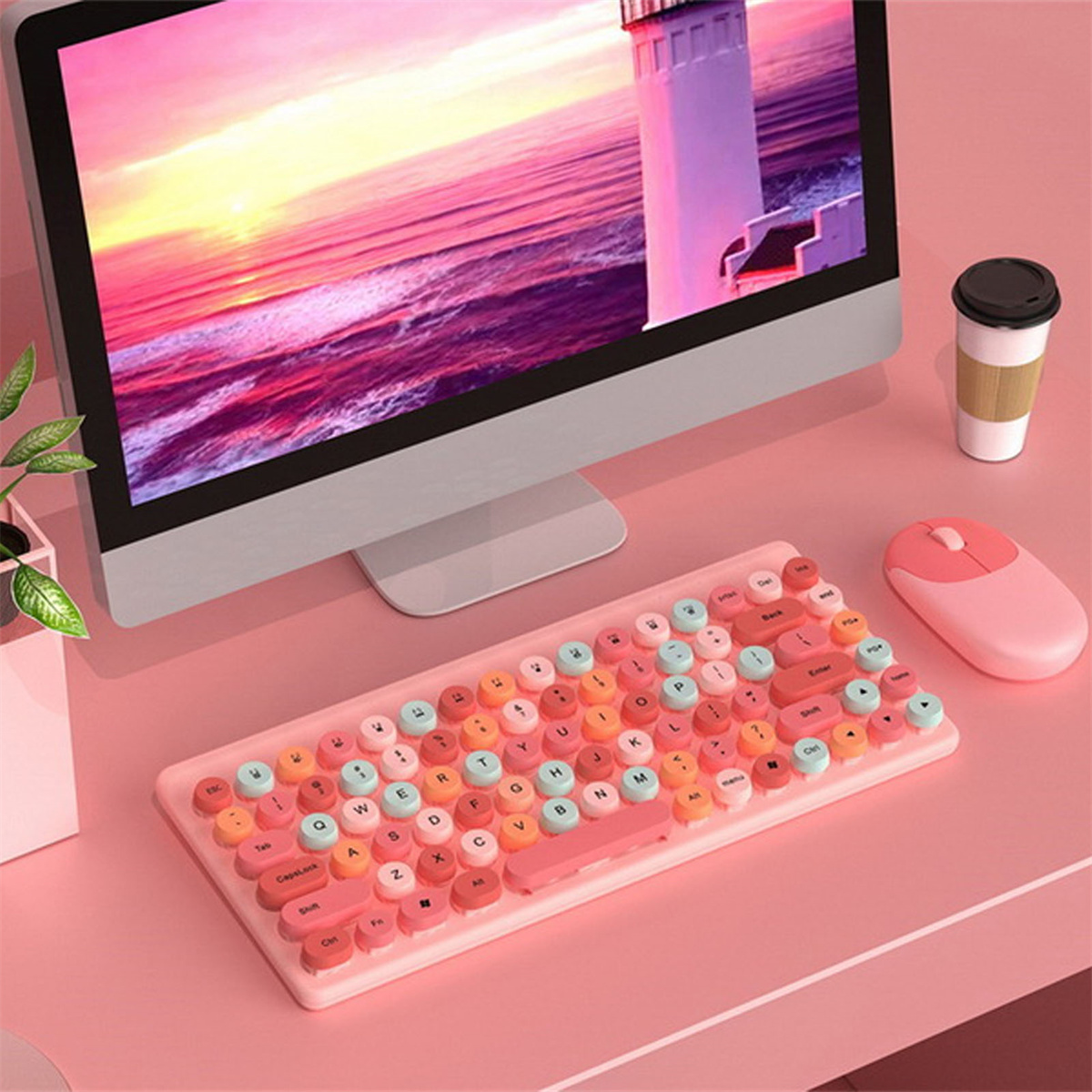 Eine rosa Tastatur mit runden Tasten, eine rosa Maus und eine schwarze Kaffeetasse auf einem rosa Schreibtisch.