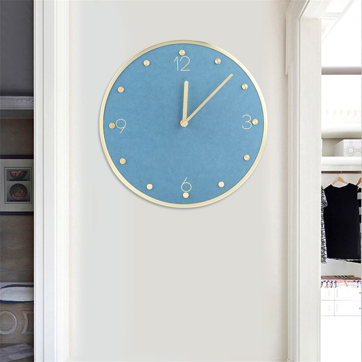 Eine blaue Wanduhr mit goldenem Rand. Die Uhr zeigt die Zeit an und ist an einer weißen Wand montiert. Hinten ist eine Tür.