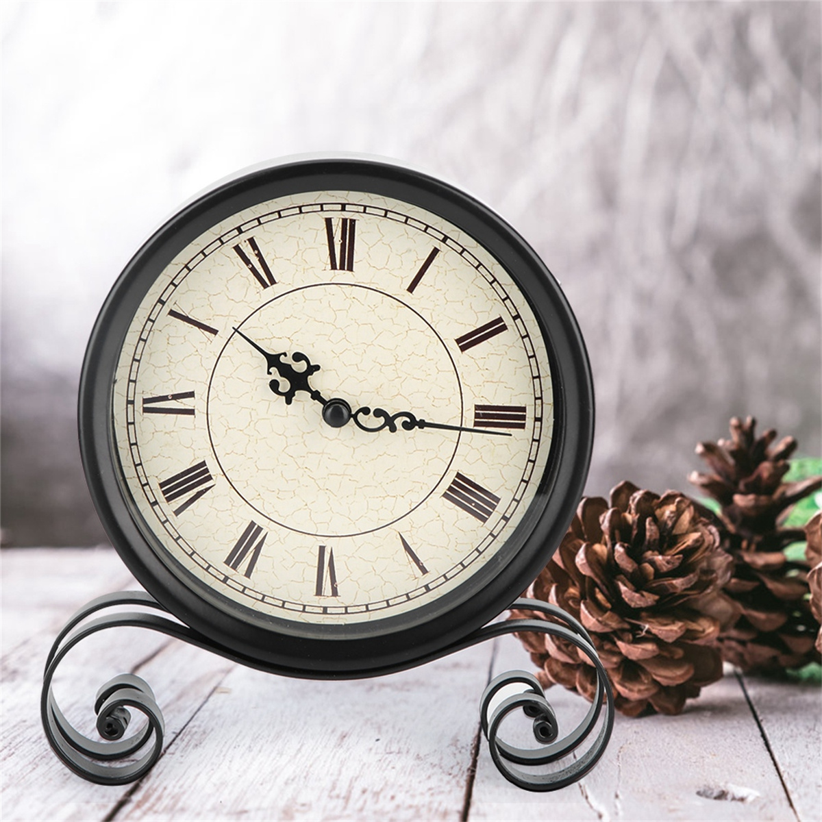 Schwarze Uhr auf einem Ständer, mit Tannenzapfen davor. Die Uhr zeigt römische Ziffern an.
