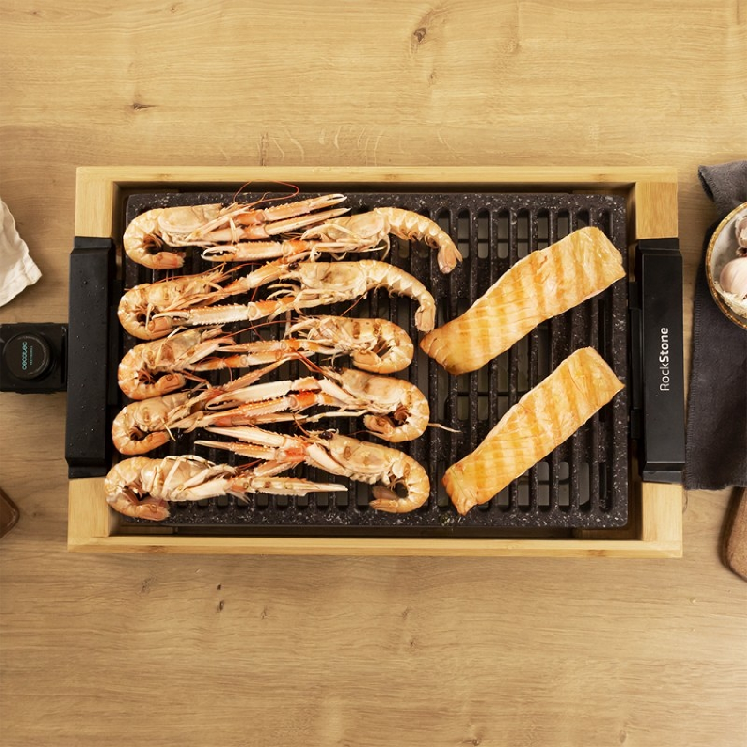 Una parrilla de madera con gambas y salmón cocidos encima, colocada sobre una superficie de madera. Vista superior.