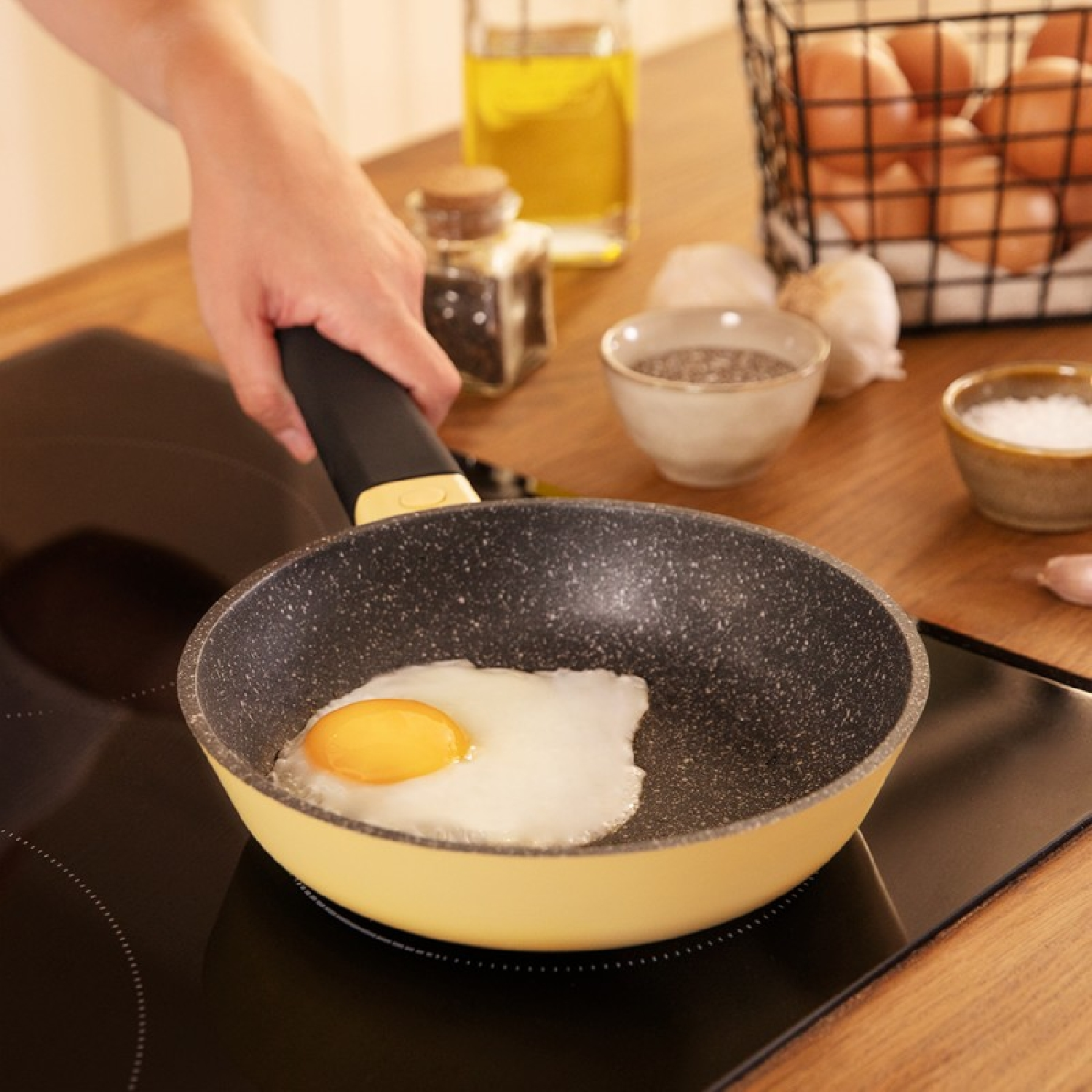 Gebakken ei in een gele pan met steenachtige textuur, naast ingrediënten op een zwart fornuis.