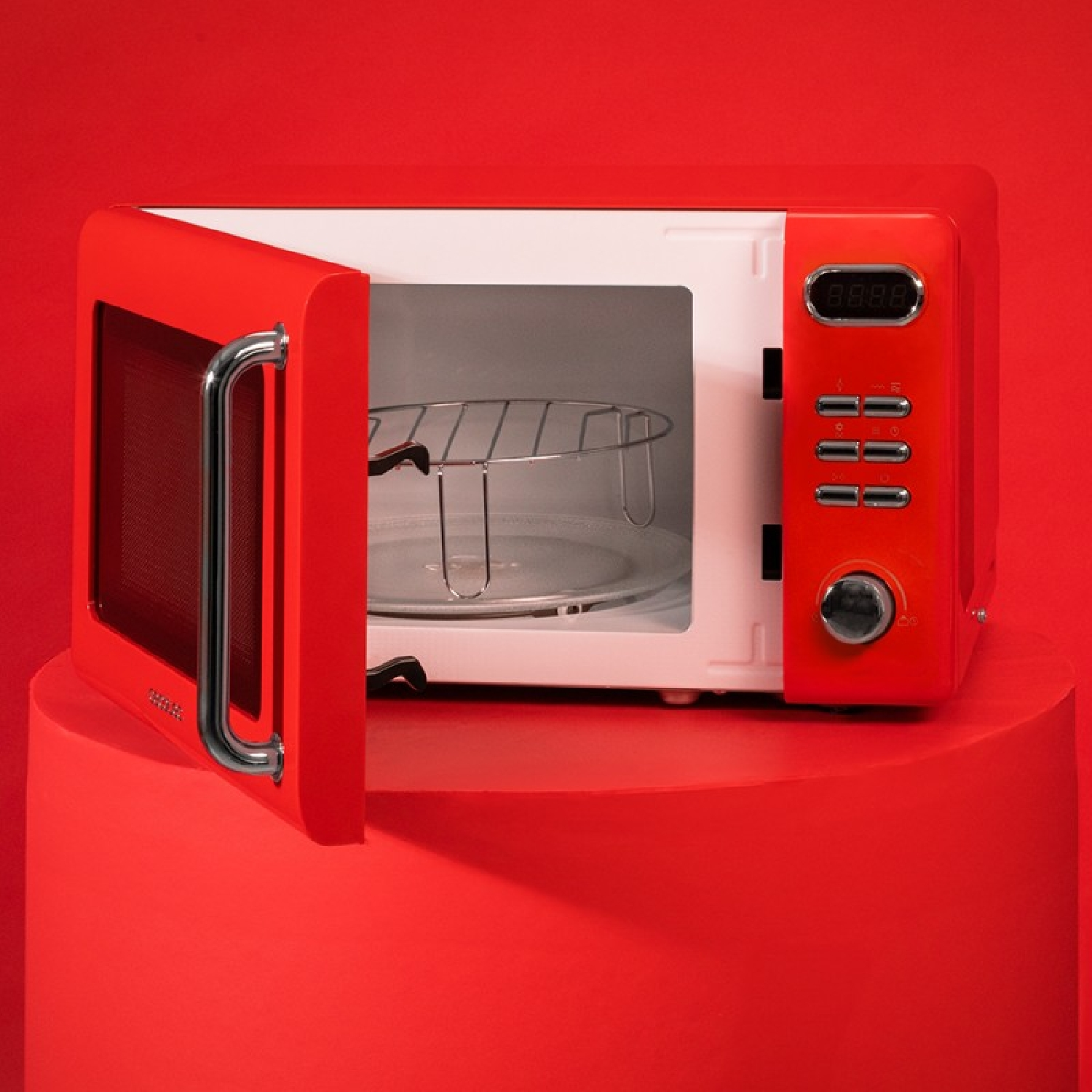 Czerwona kuchenka mikrofalowa z otwartymi drzwiami na czerwonym cokole. Widoczne wnętrze. Wyświetlacz cyfrowy z prawej.
