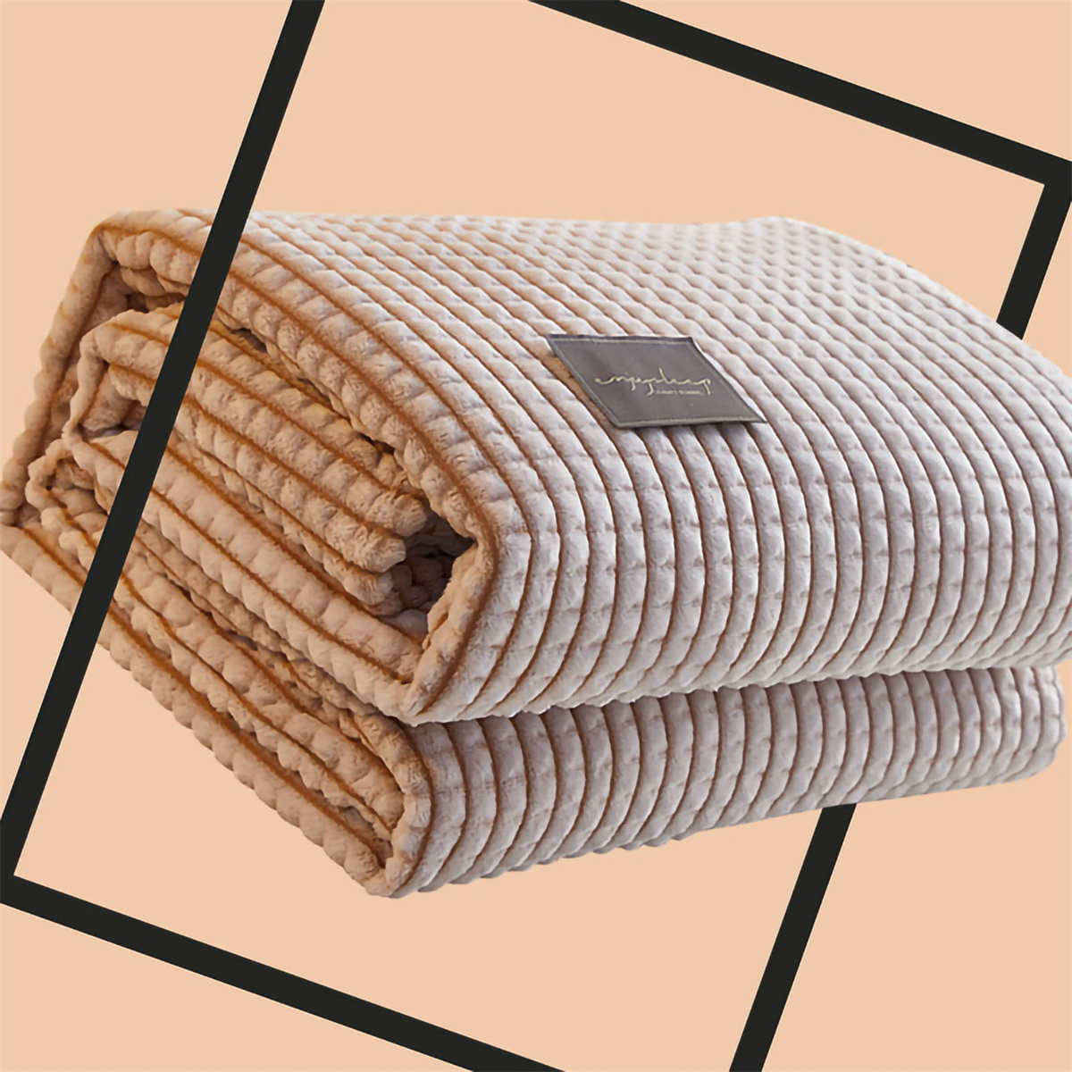 Gefaltete beige Corddecke mit Etikett in schwarzem Rahmen vor Pfirsichhintergrund.
