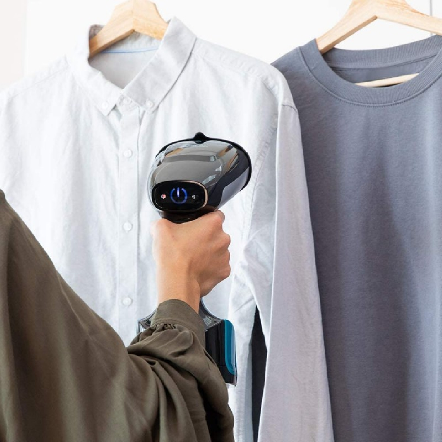 Una persona usando un vaporizador portátil en una camisa blanca. Una camisa gris cuelga a la derecha.