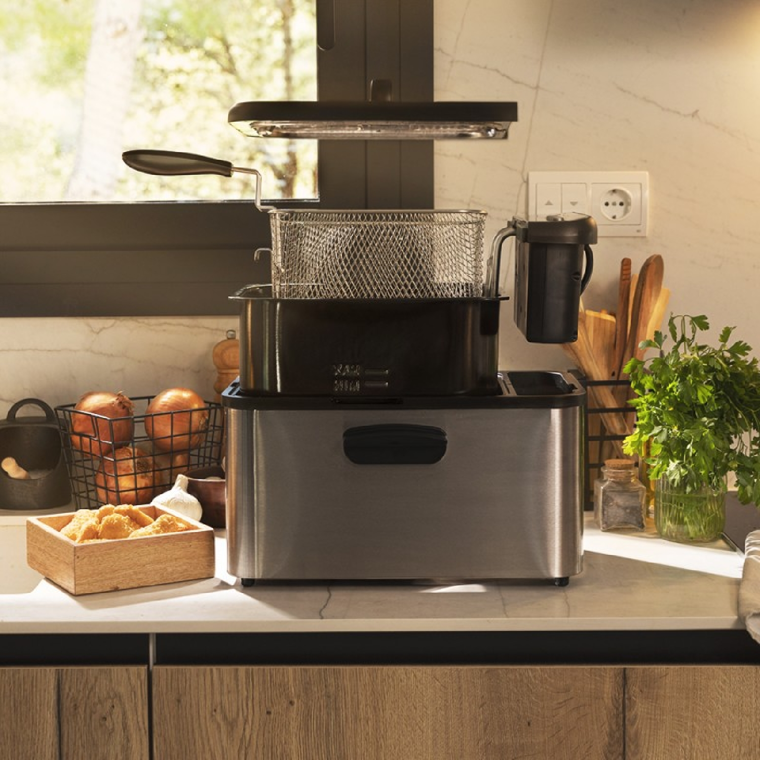 Frytownica ze stali nierdzewnej na blacie. Kosz z cebulą i drewniane pudełko z jedzeniem z przodu.