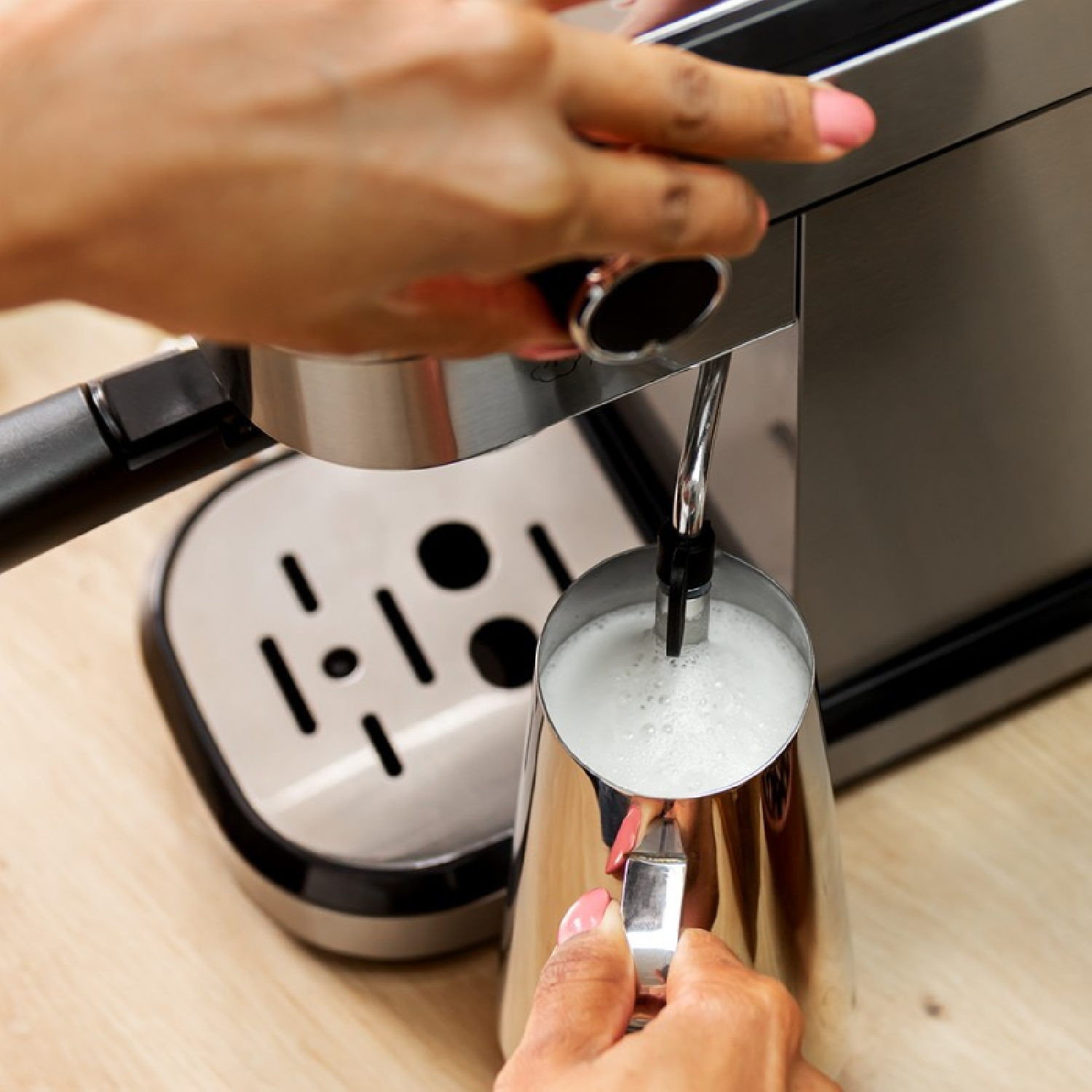 Osoba korzysta z ekspresu do kawy, spieniając mleko w dzbanku ze stali nierdzewnej.