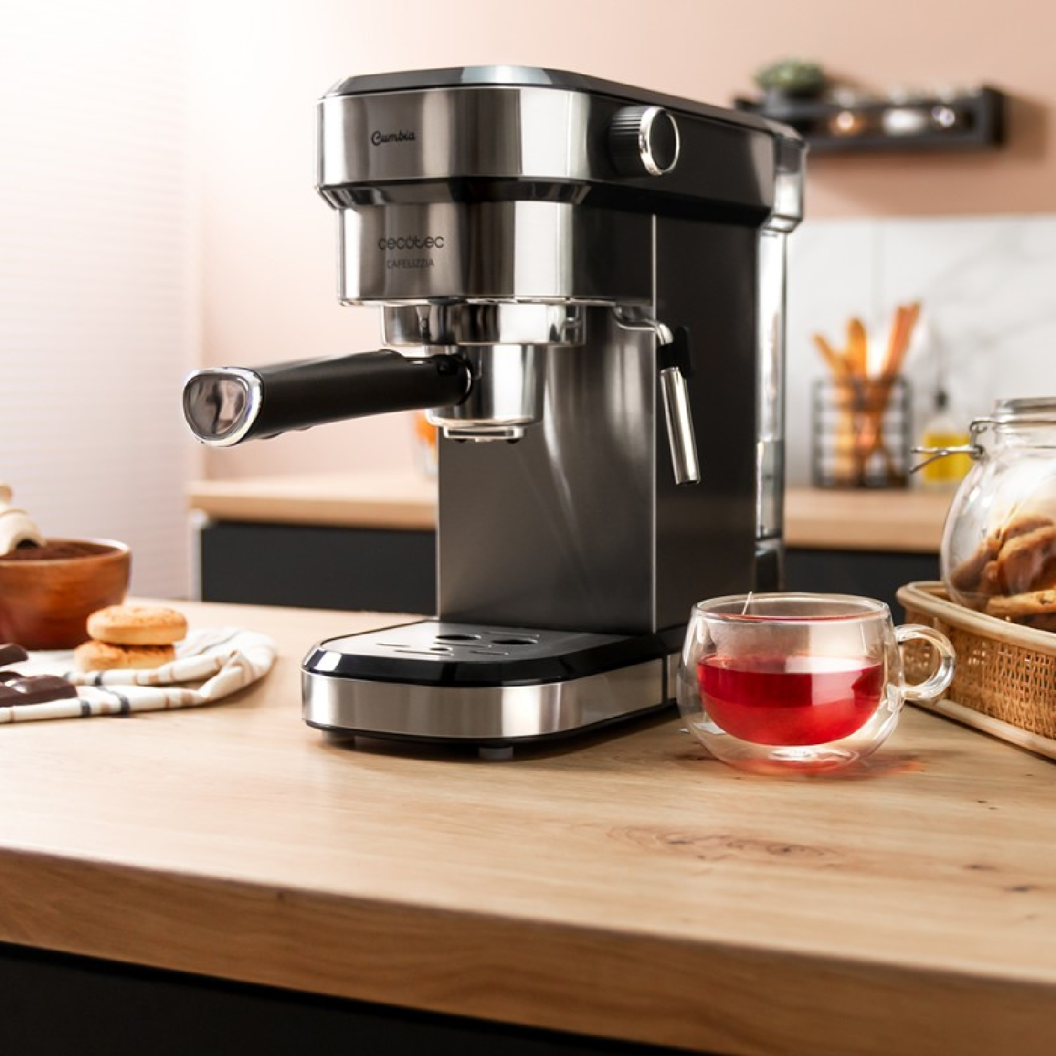 Czarny i srebrny ekspres do espresso. Szklanka z czerwoną cieczą. Drewniany stół.