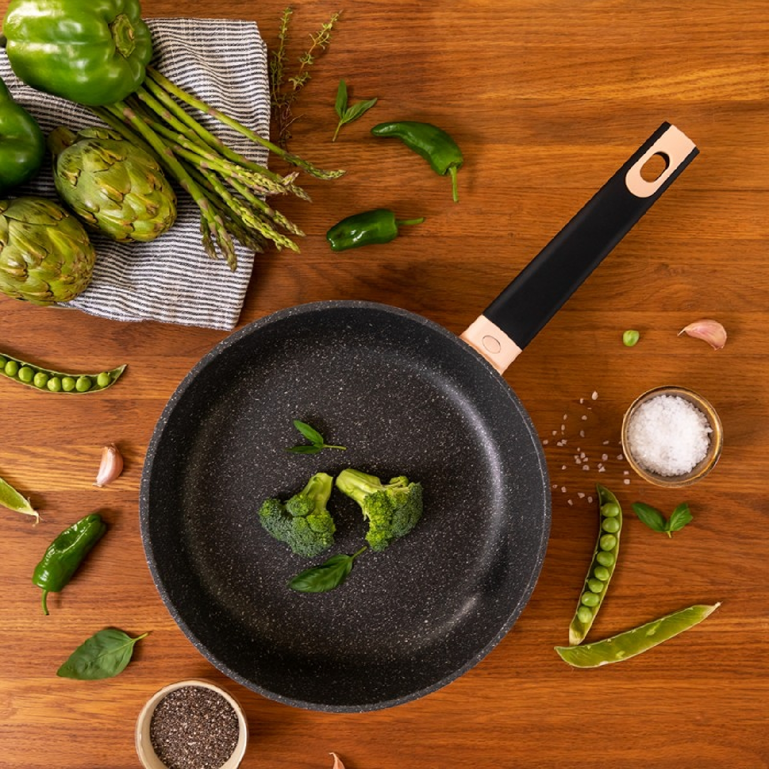 Bovenaanzicht van een pan, broccoli, paprika's en andere groenten op een houten tafel.