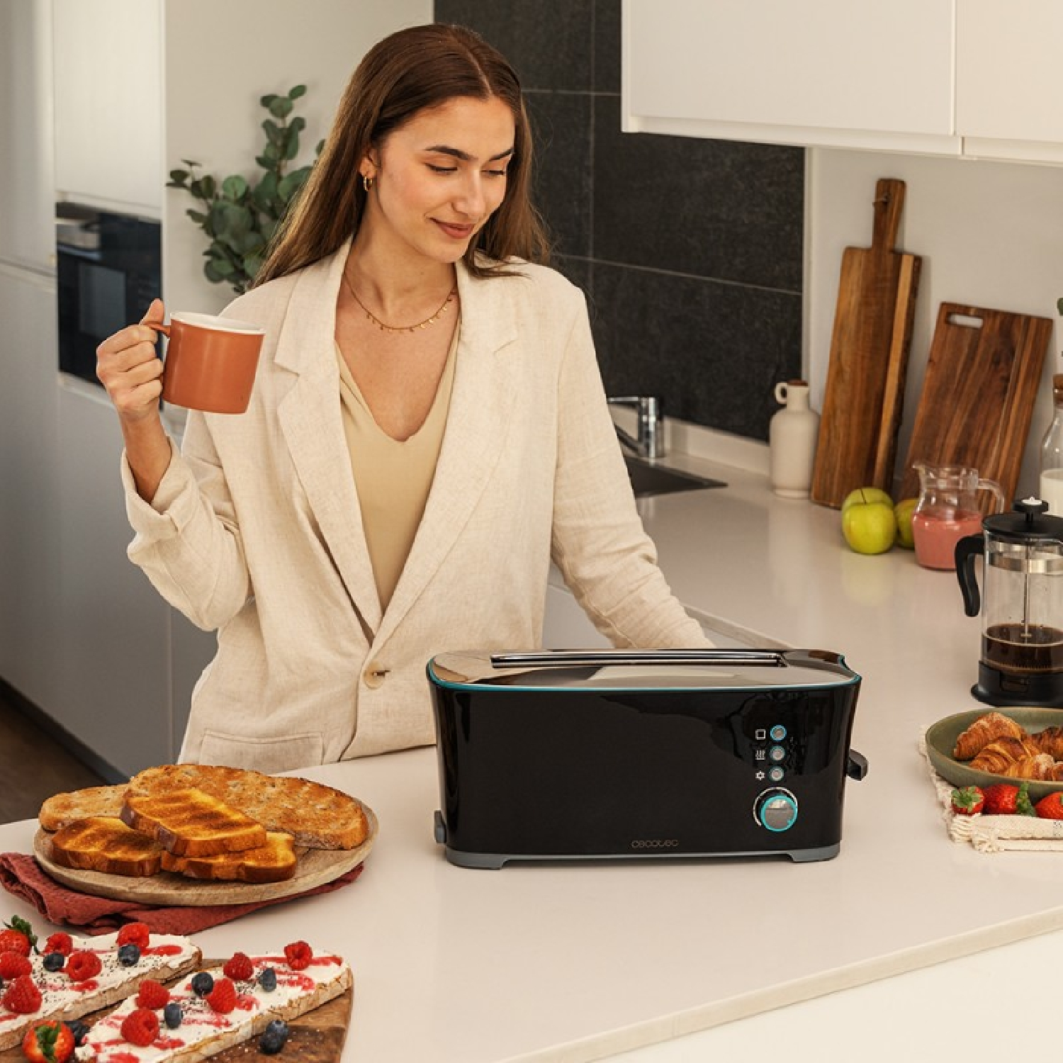 Una donna sorride, tiene una tazza, vicino a un tostapane con toast e altri cibi per la colazione.