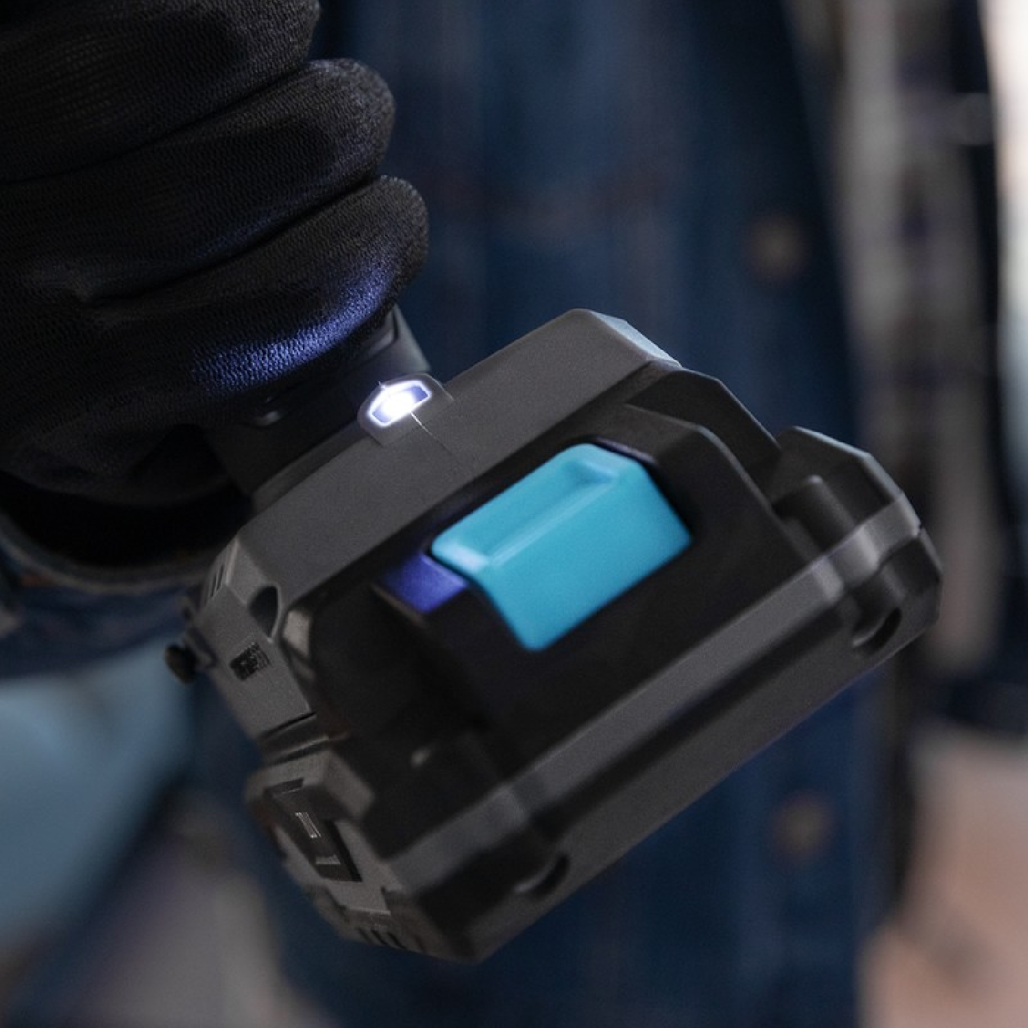 Dłoń trzymająca elektronarzędzie. Czarno-niebieskie narzędzie z czarną rękawicą. Rozmyte tło.