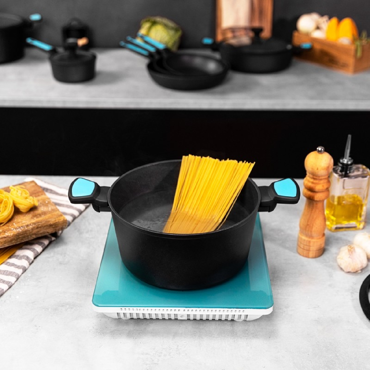 Espaguetis en una olla negra sobre una encimera verde azulado. Otros utensilios de cocina son visibles.
