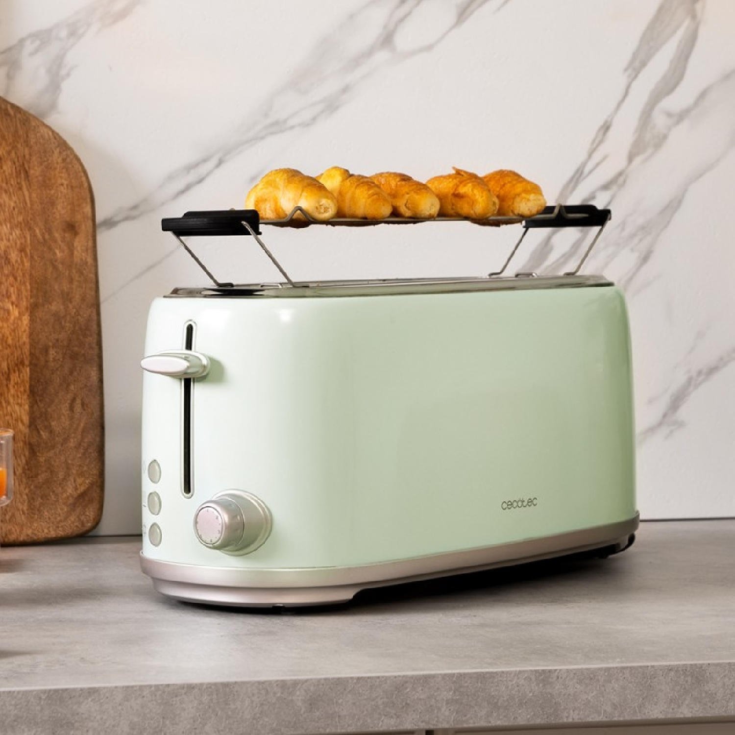 Grüner Toaster mit Croissants oben drauf, steht auf einer grauen Arbeitsplatte neben einem Holzbrett.