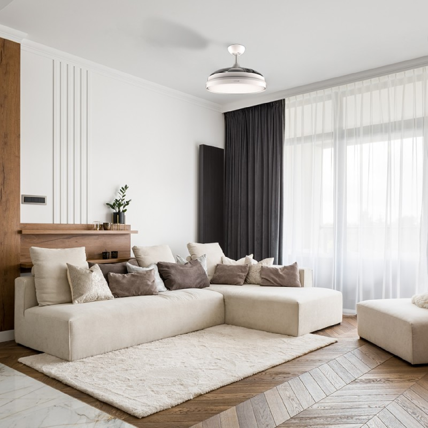 Nowoczesny salon z beżową sofą, dywanem i wentylatorem sufitowym. Widoczne okno z zasłonami.