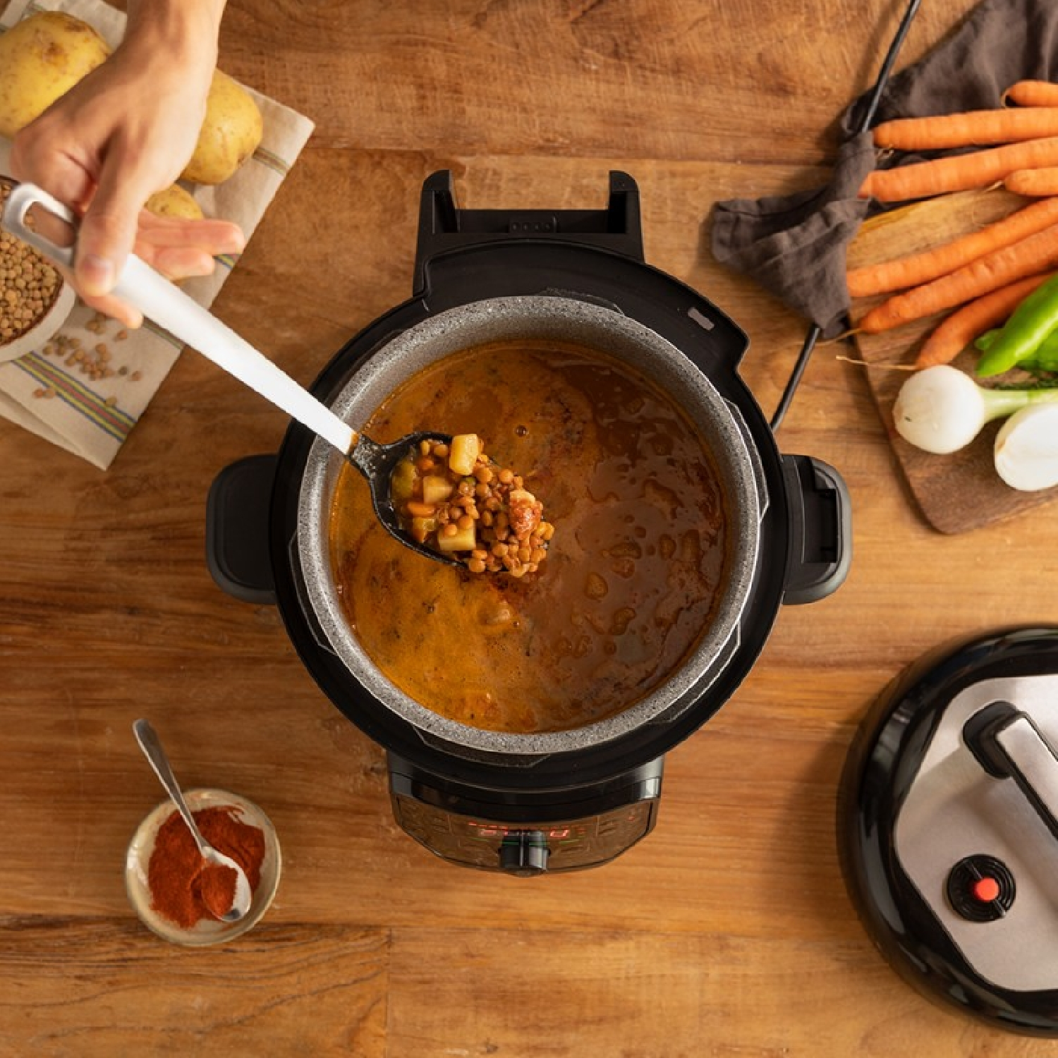Una olla con sopa que se sirve con una cuchara. Las verduras y patatas lo rodean. Otros ingredientes cerca.