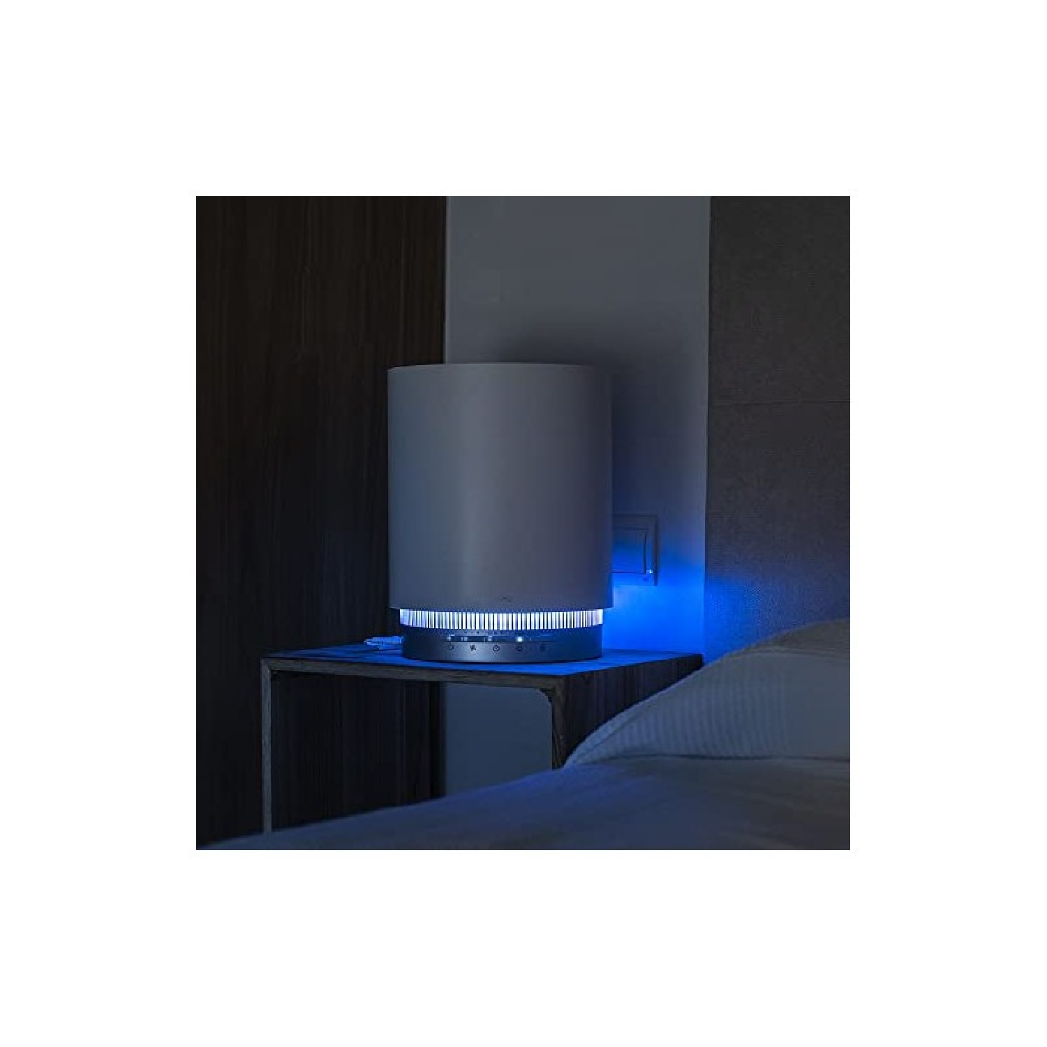 Lampada cilindrica bianca con base luminosa blu su un comodino. Ambiente buio.