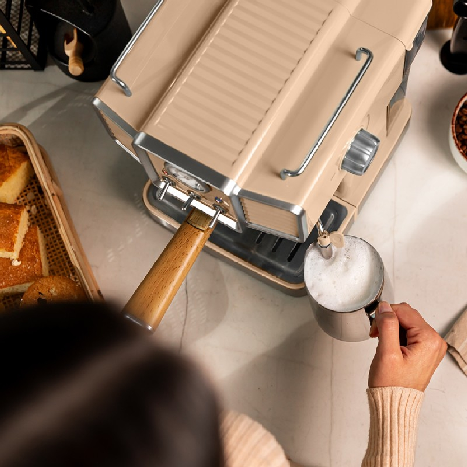 Persona che fa schiuma con una macchina per espresso beige. Un manico in legno, una tazza e ingredienti sono visibili.