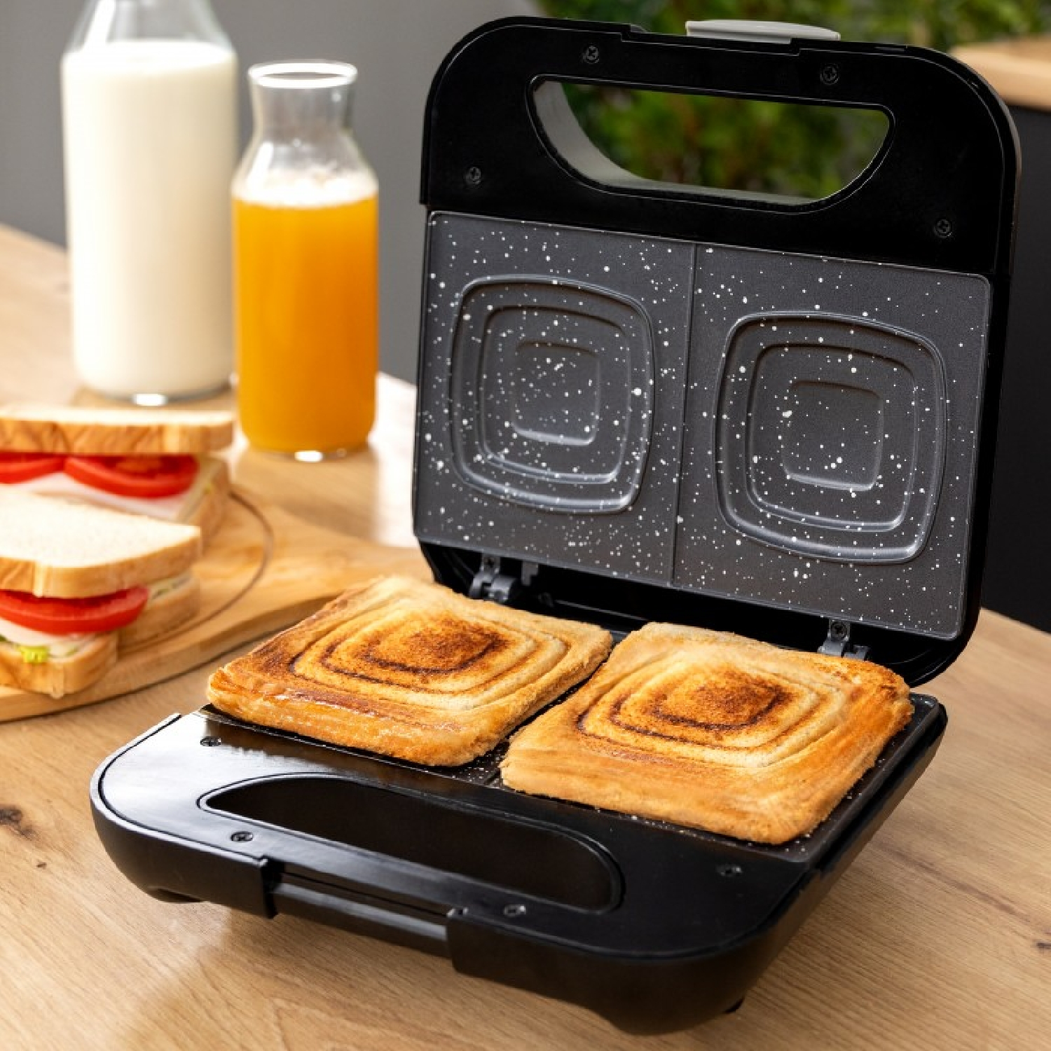 Sandwichmaker met twee geroosterde sandwiches erin. Een fles melk en sinaasappelsap staan ernaast.