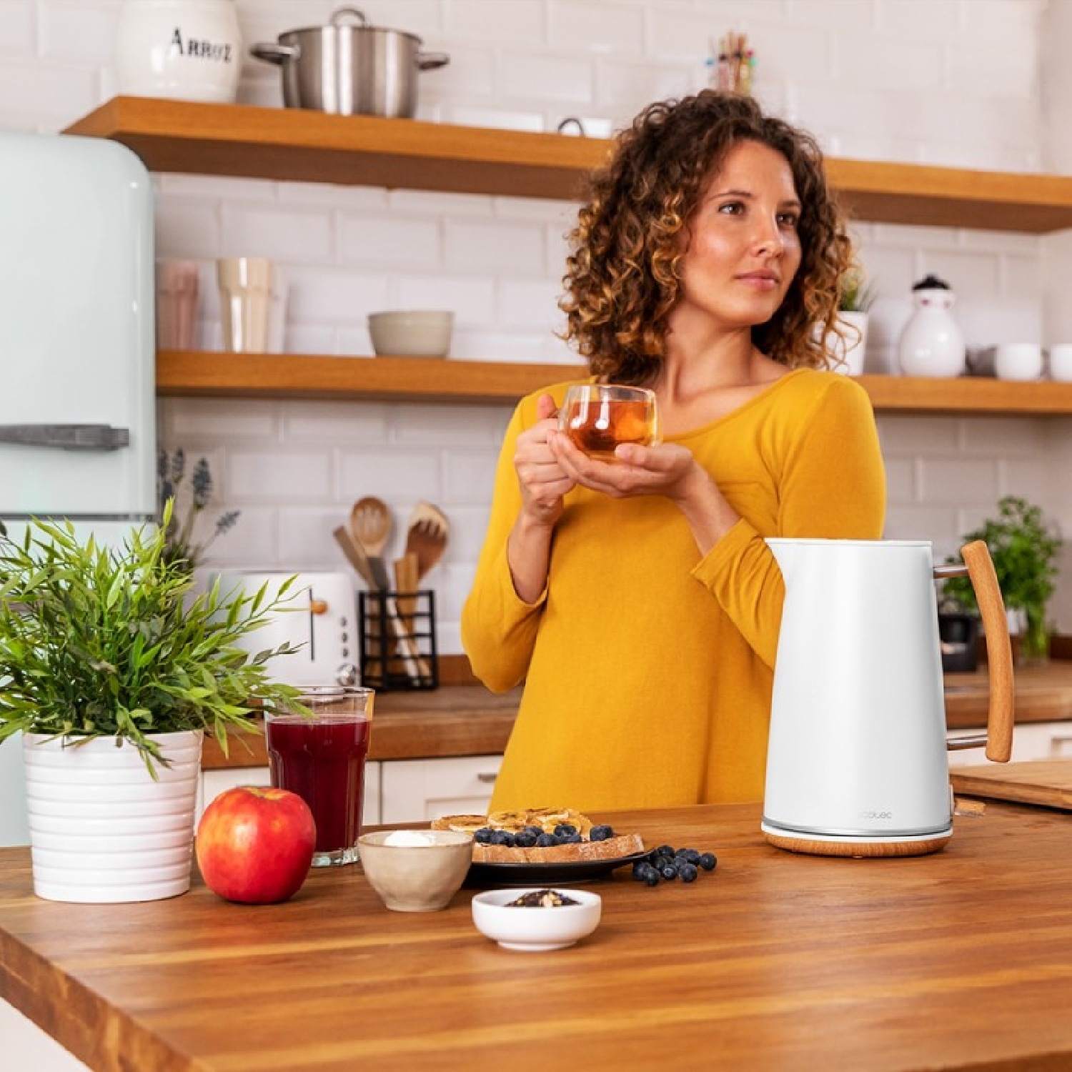 Kobieta trzymająca filiżankę herbaty na drewnianym stole. Jedzenie i czajnik.