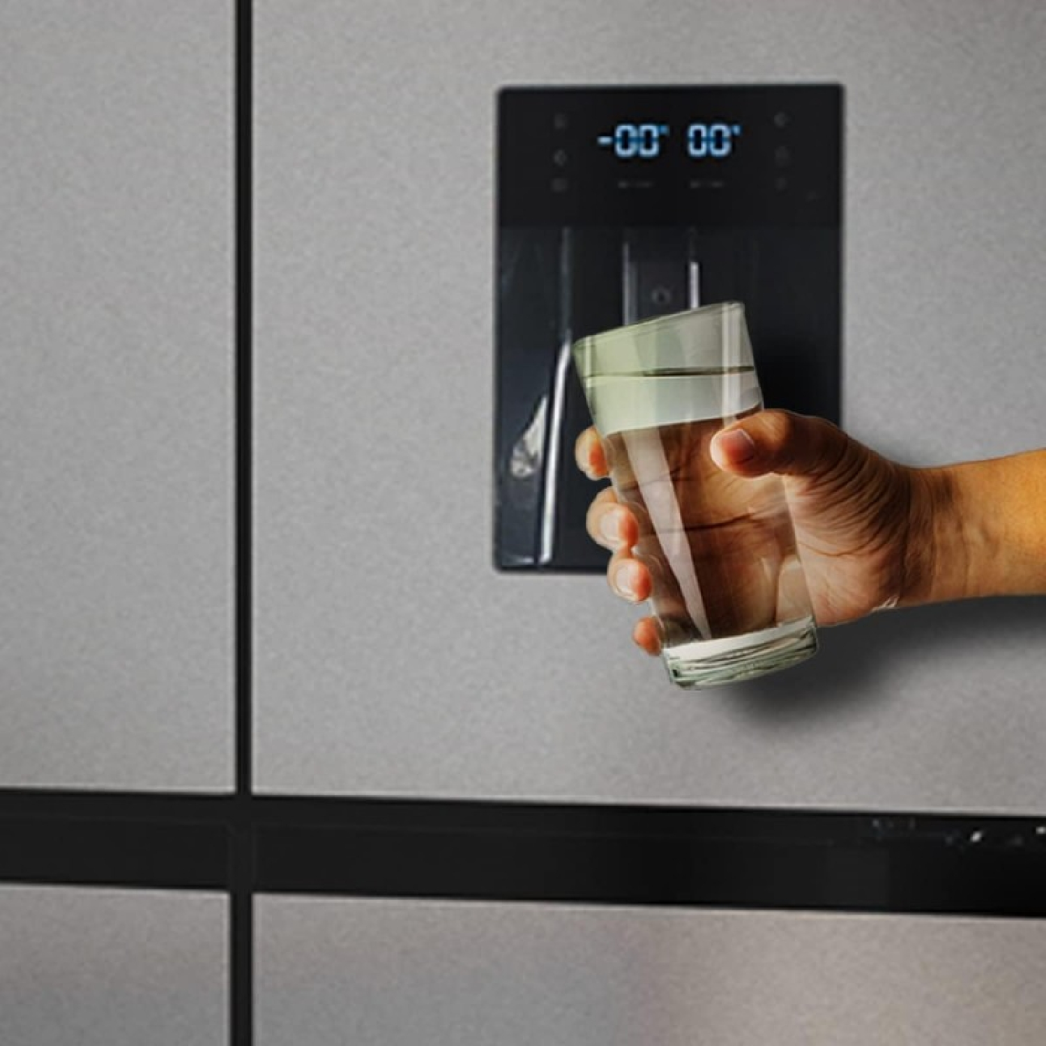 Osoba trzymająca szklankę wody przed lodówką ze stali nierdzewnej. Woda jest czysta.