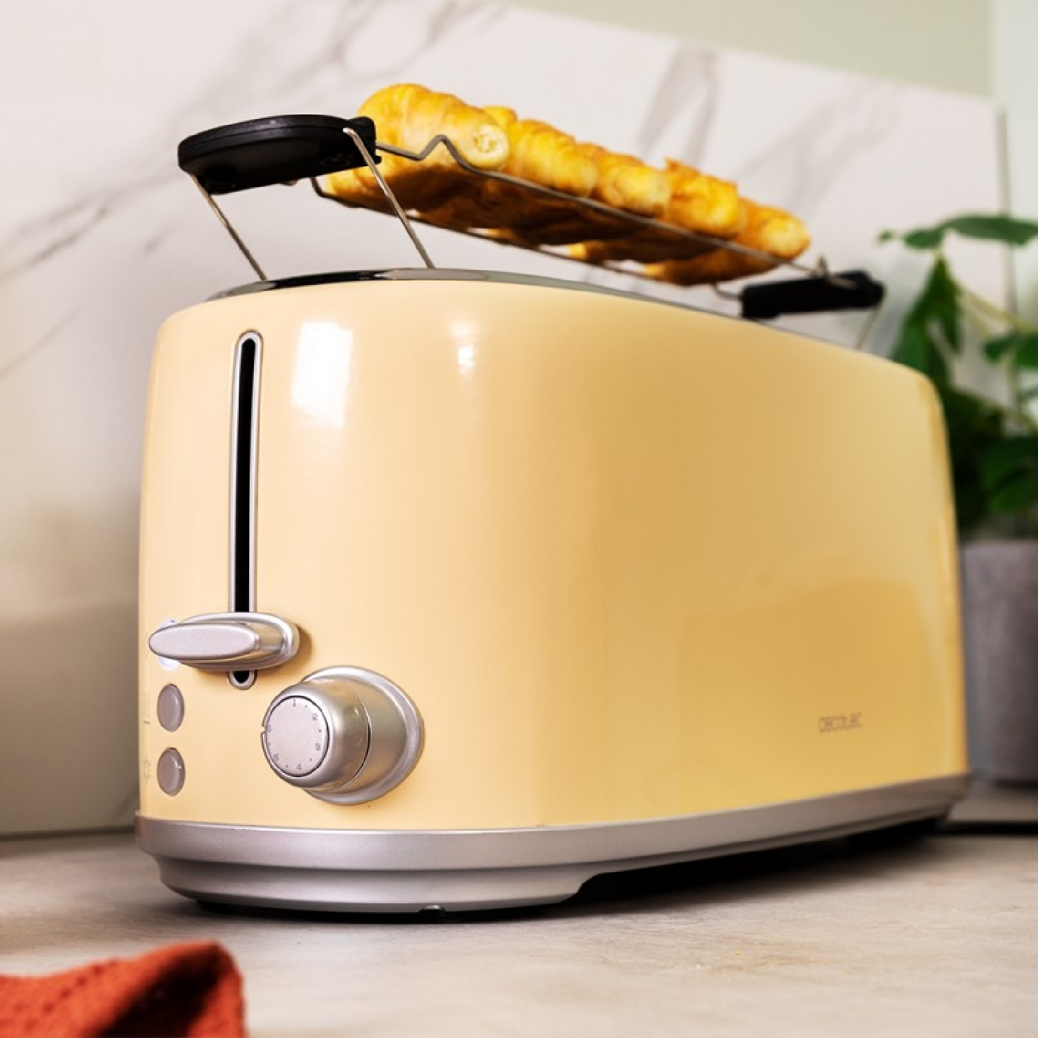 Ein beiger Retro-Toaster mit Croissants oben drauf. Er steht in der Nähe einer Pflanze und einer Marmorwand.