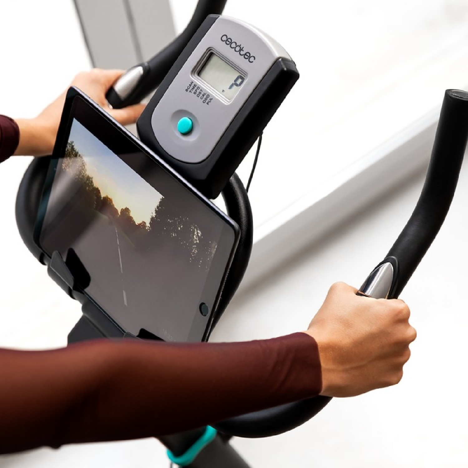 Mani che tengono un tablet su una cyclette. Lo schermo mostra una strada.