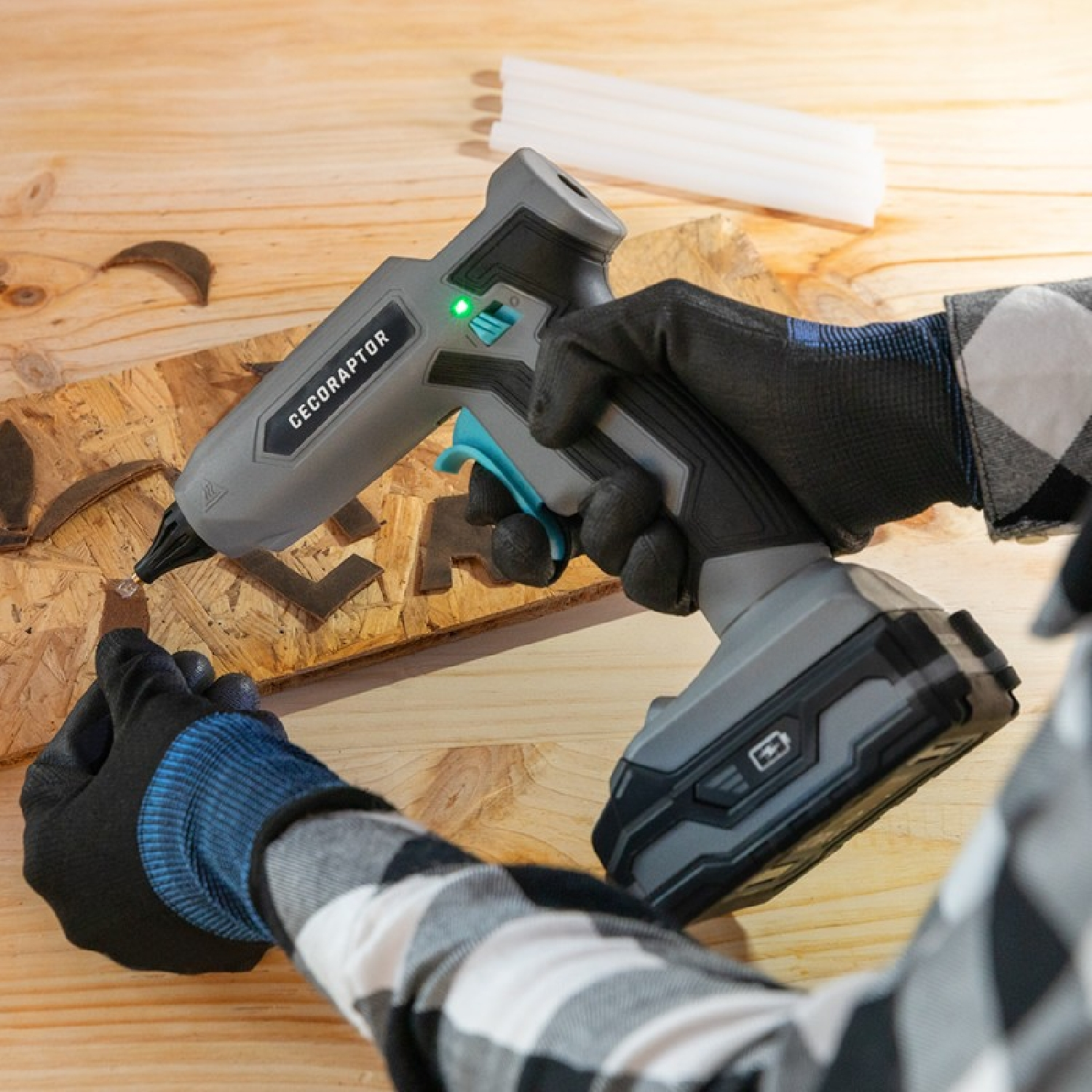 Osoba w rękawicach używa pistoletu do klejenia na drewnie. Pistolet jest szary i czarny, w pobliżu znajdują się sztyfty kleju.