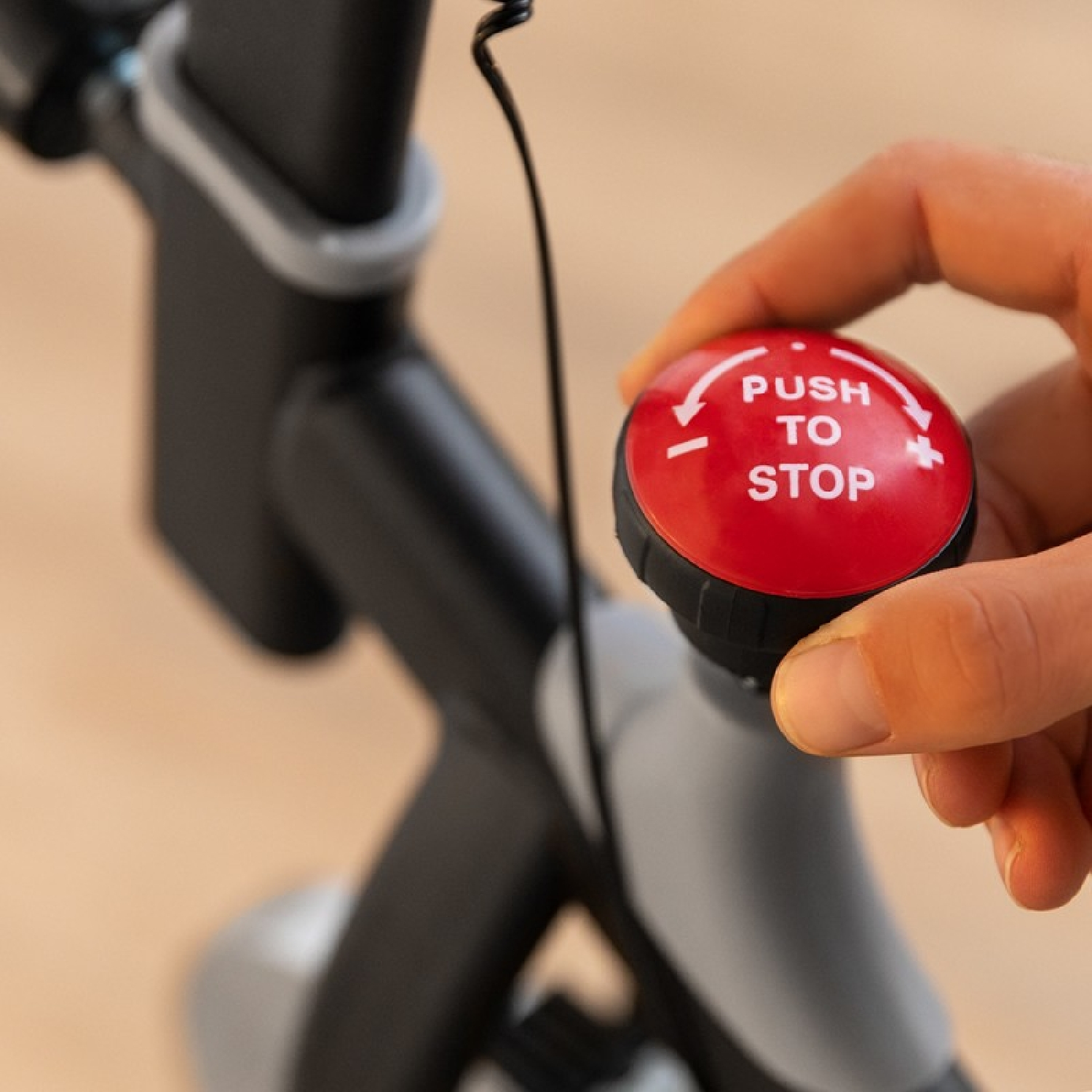 Mano che preme un pulsante rosso con scritto 'PUSH TO STOP' su un attrezzo grigio. Primo piano.
