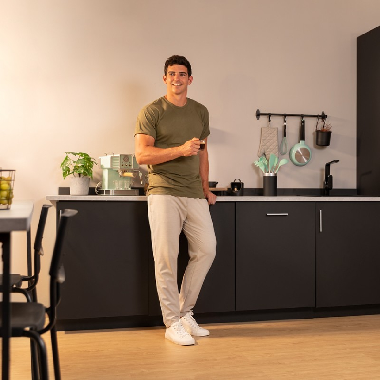 Un uomo in cucina tiene una tazza. C'è una macchina per il caffè e un bancone.