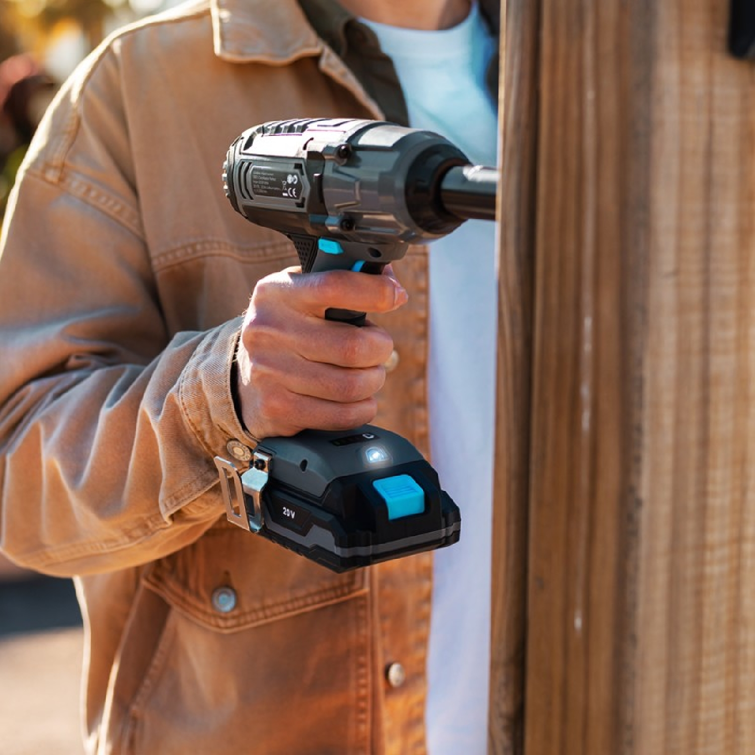 Osoba używająca czarno-niebieskiej bezprzewodowej wkrętarki udarowej na drewnianym płocie.