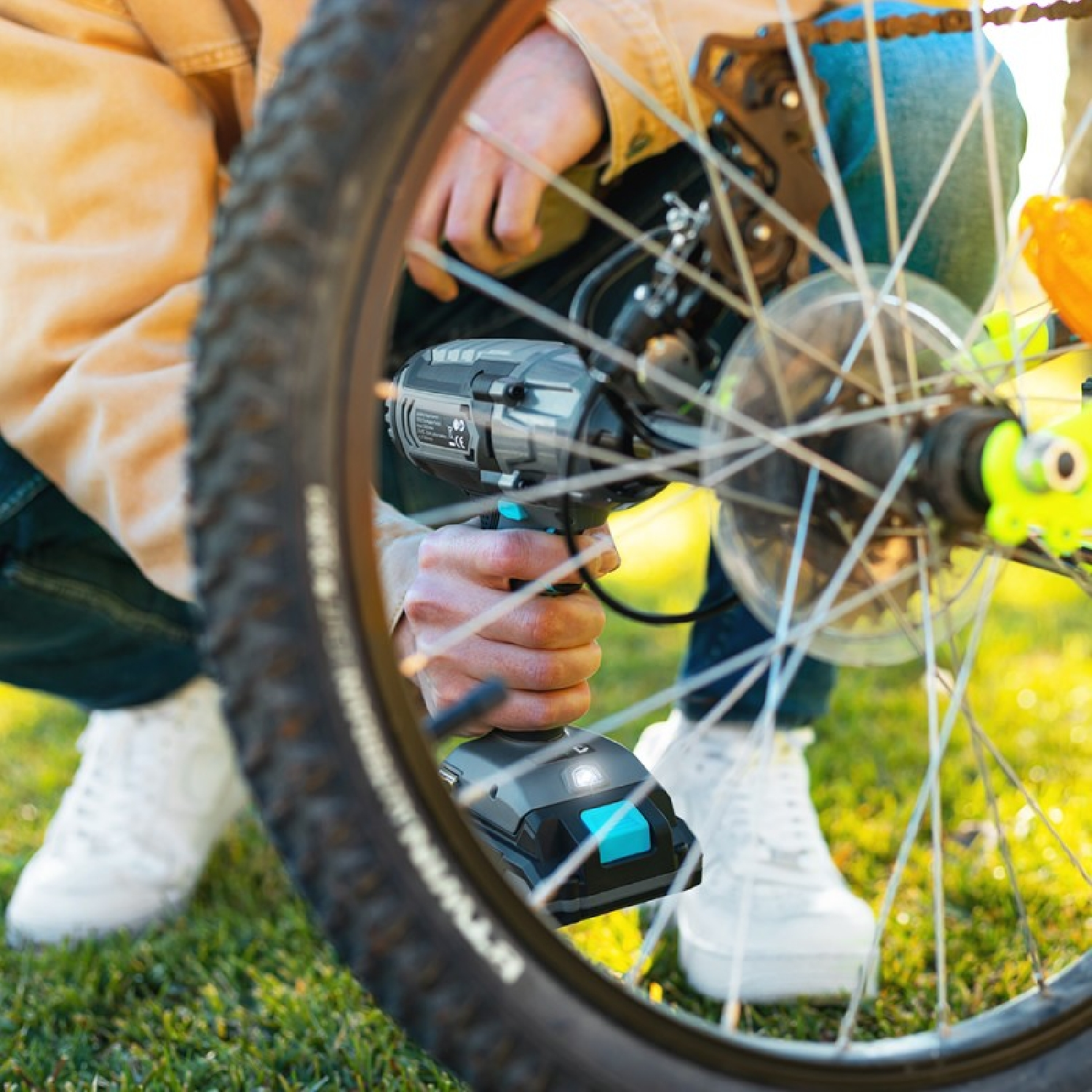 Osoba używająca wiertarki na kole roweru. Tło z zieloną trawą.