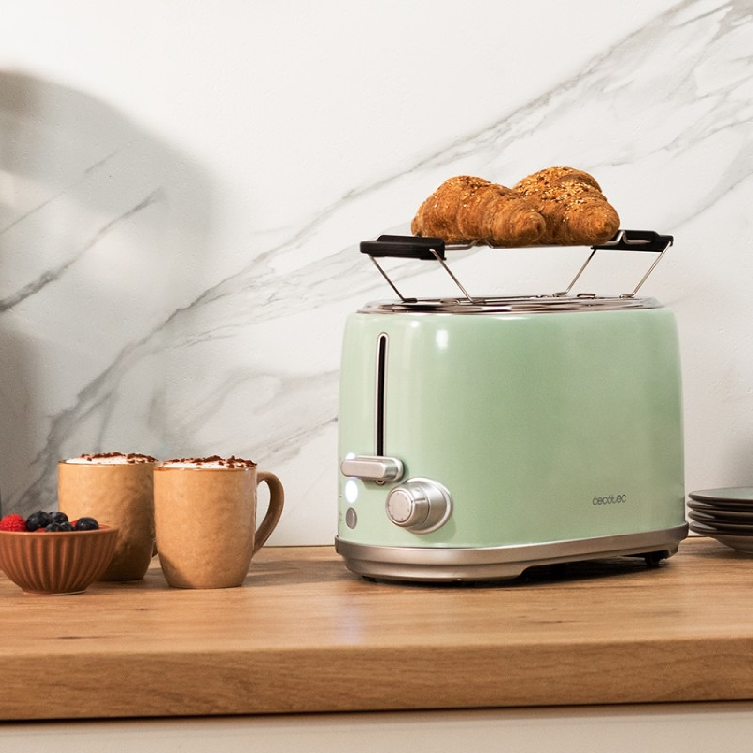 Un tostapane verde con croissant sopra. Due tazze di caffè e una ciotola di bacche sono vicine.