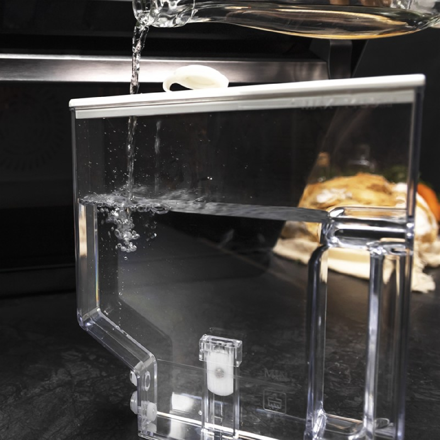 Agua vertiéndose en un recipiente de plástico transparente desde arriba.