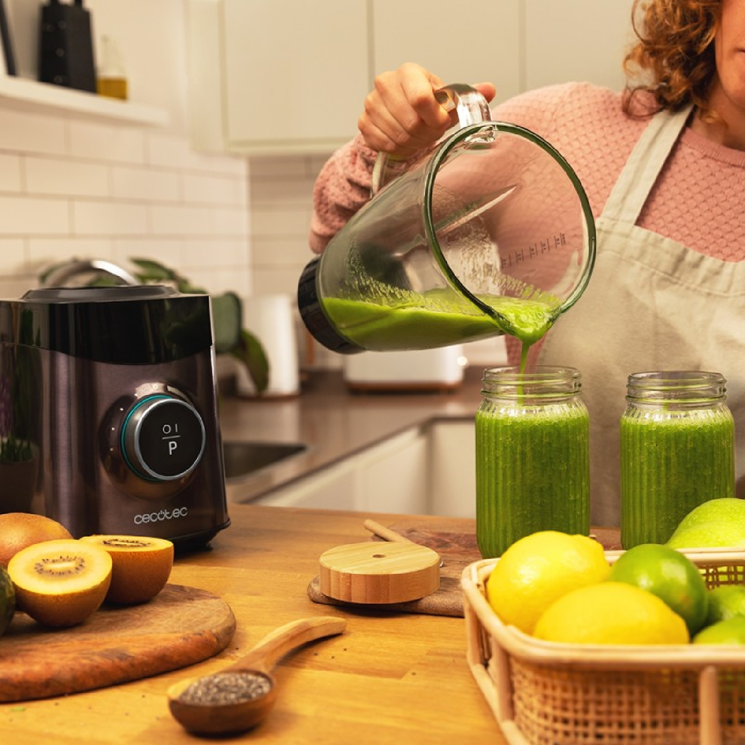 Kobieta wlewa zielone smoothie do słoików. Blender, kiwi i cytryny na drewnianym blacie.