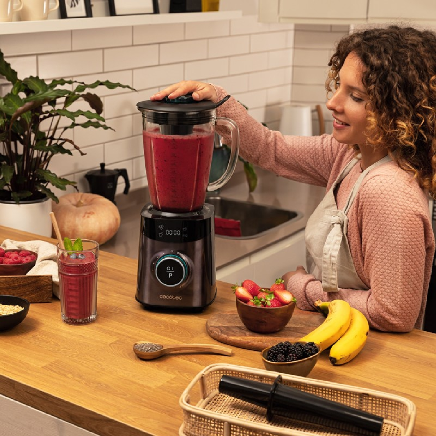 Kobieta robi koktajl blenderem, na stole truskawki i banany.